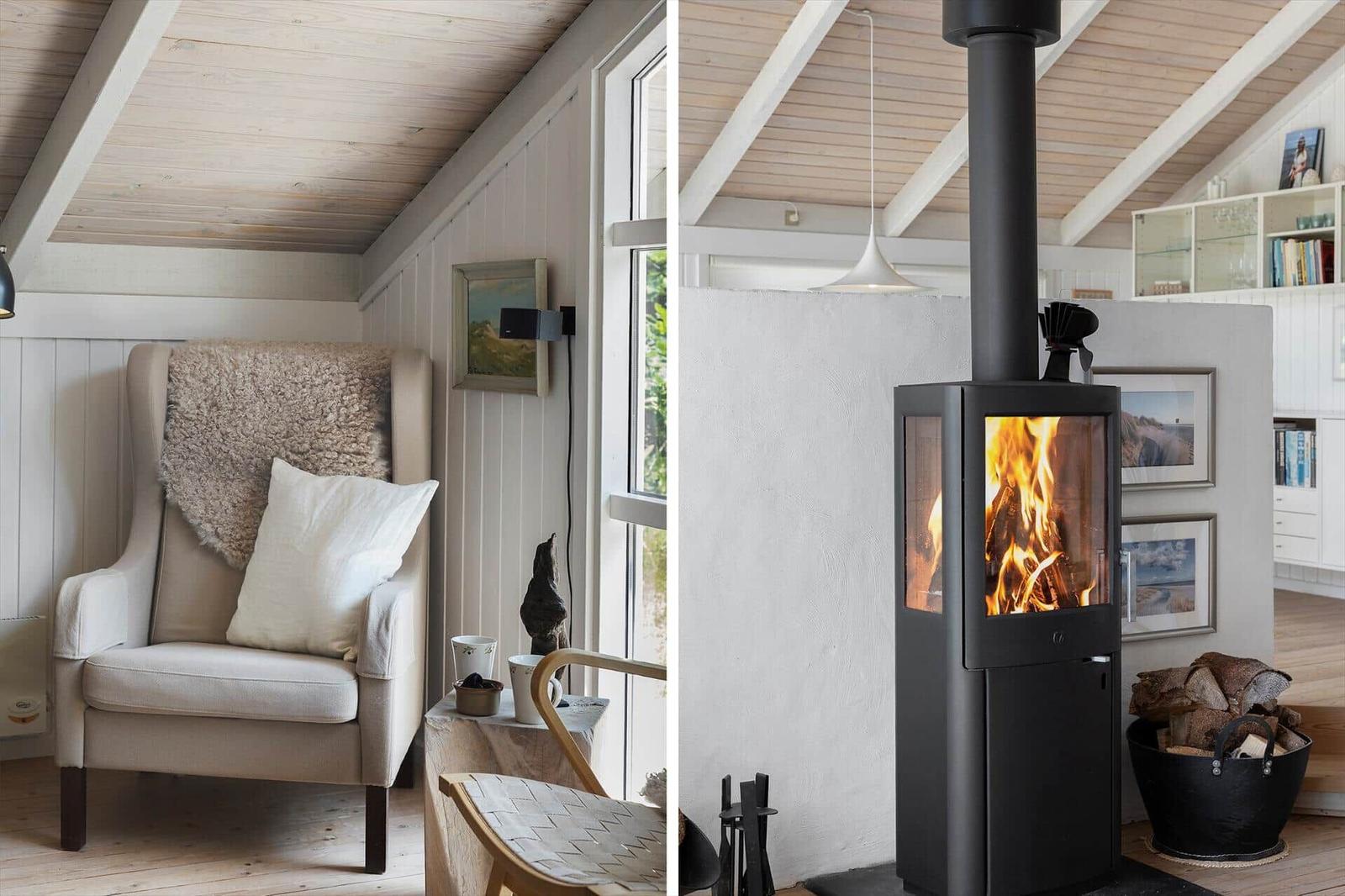 An armchair with cushions and a blanket next to a window. A fireplace with burning wood.