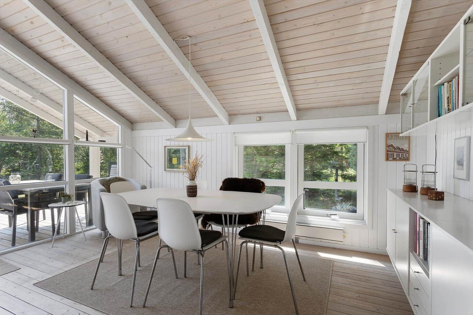 Dining area with white table and chairs, large windows, and wooden ceiling.