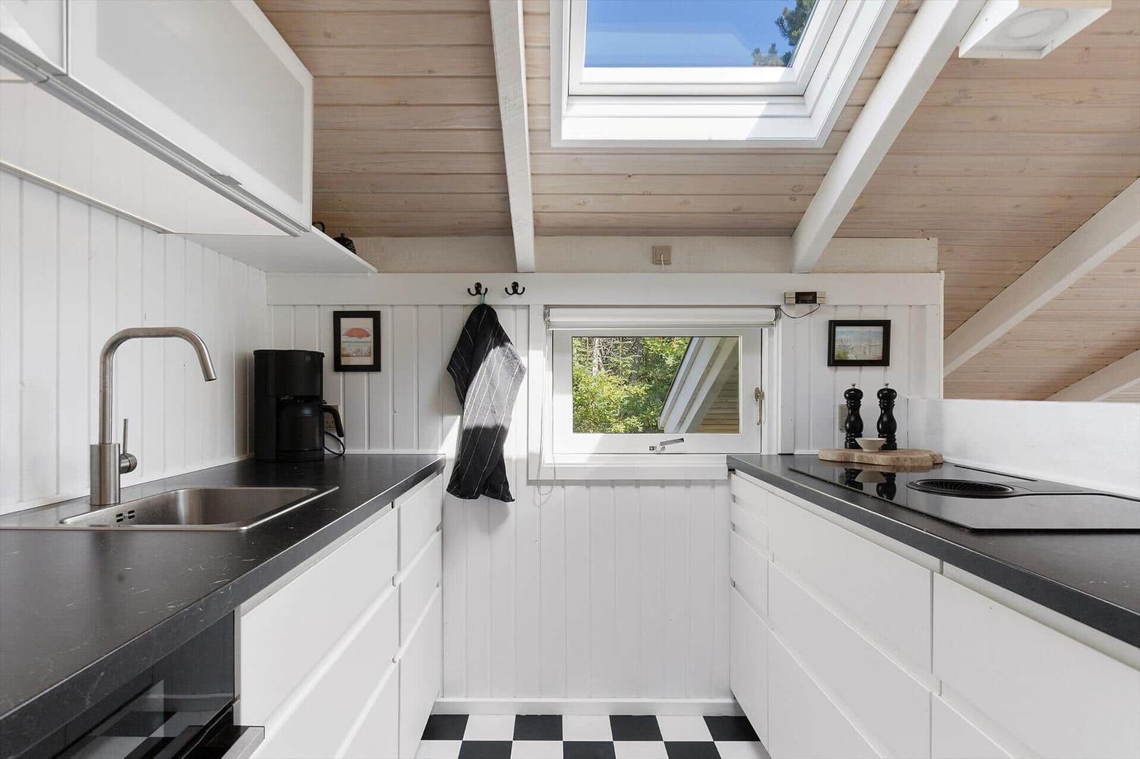 Kitchen with white cabinets, black countertops, and skylight. Black tiled floor and window with view of greenery.