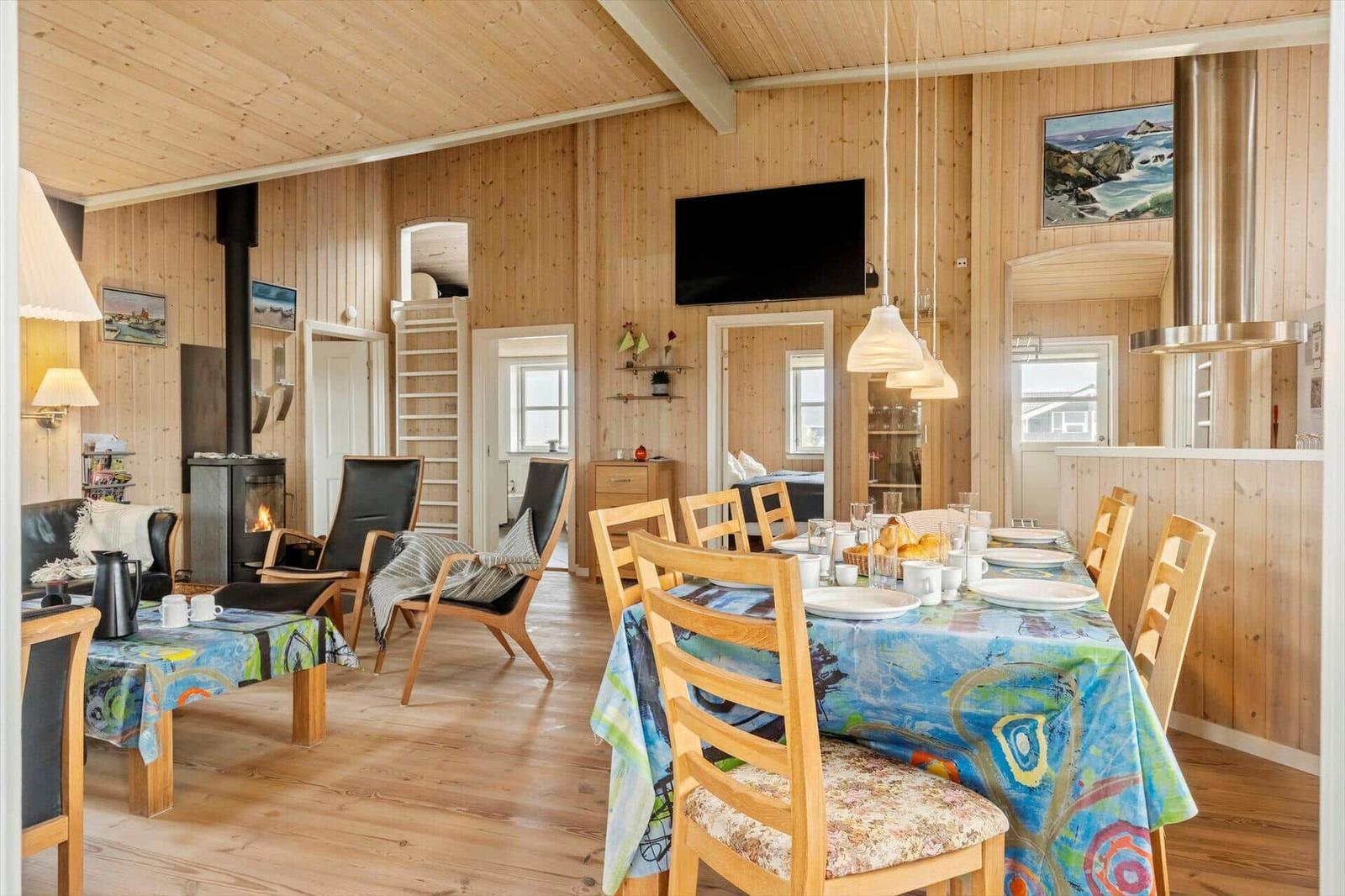 Esszimmer mit Holzwand und Esstisch, daneben Wohnbereich mit Kamin und Fernseher.