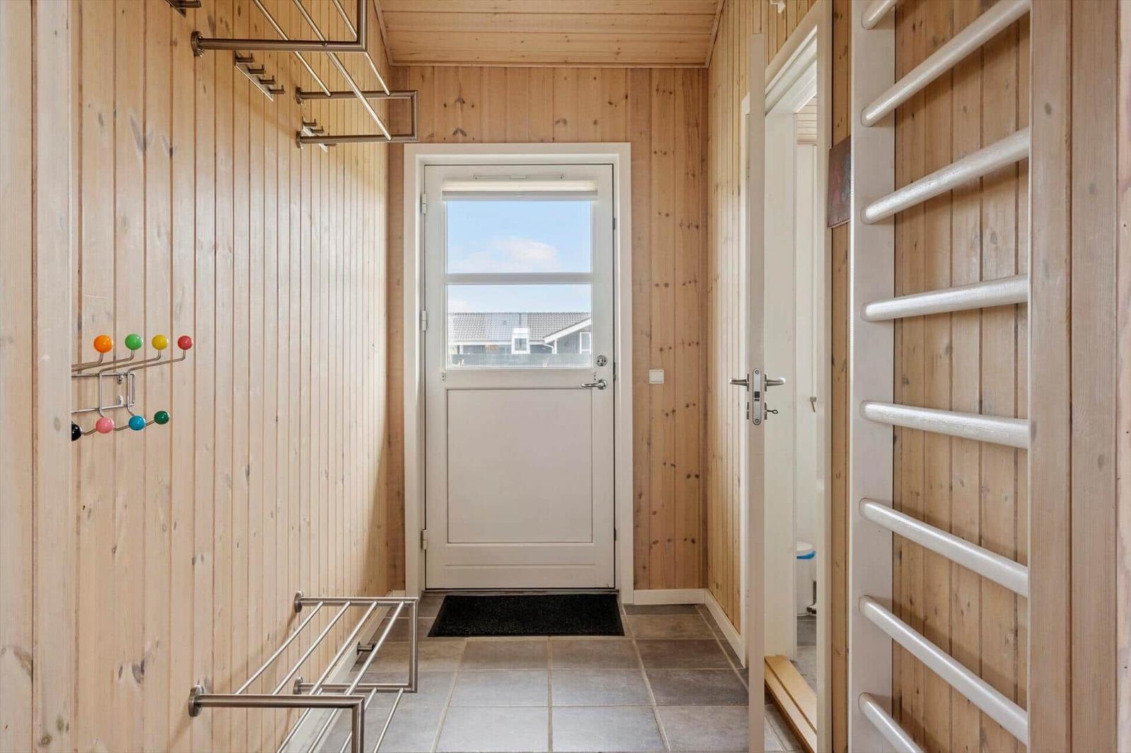 Eingangsbereich mit Holzwänden, Tür mit Fenster und Kleiderhaken.
