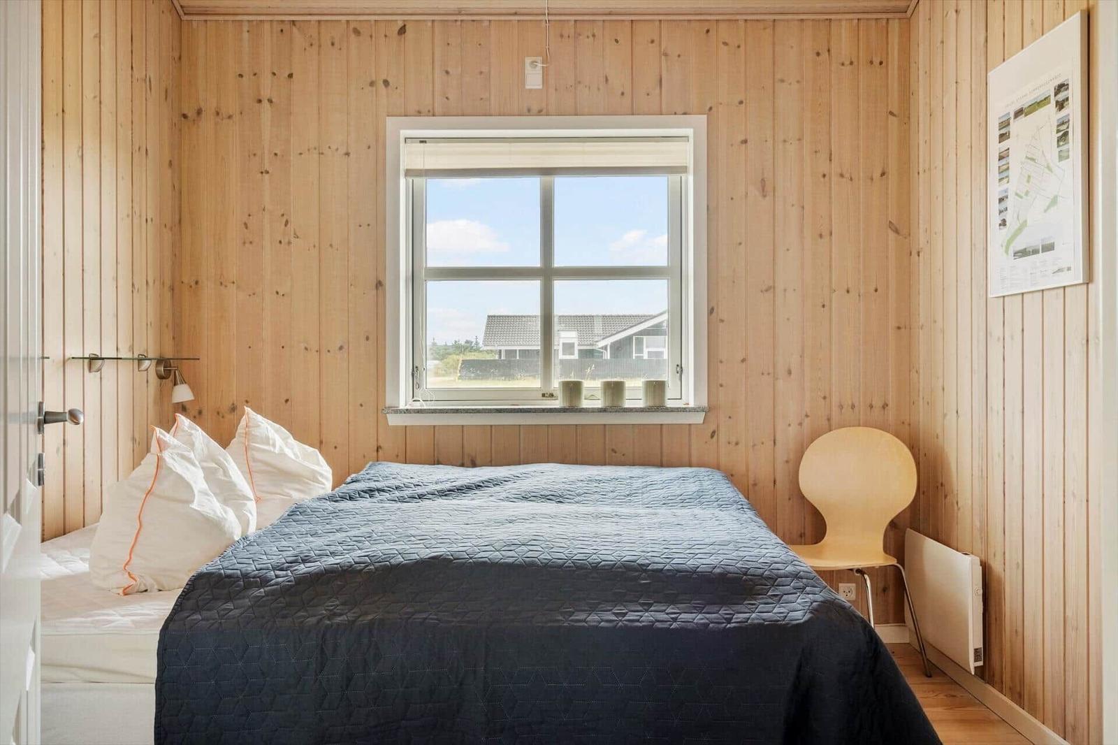 Ein Schlafzimmer mit Holzwand, Bett, Fenster und Stuhl.