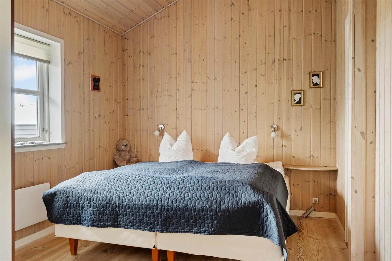 Schlafzimmer mit Holzwand, Bett mit blauer Decke und Fenster.