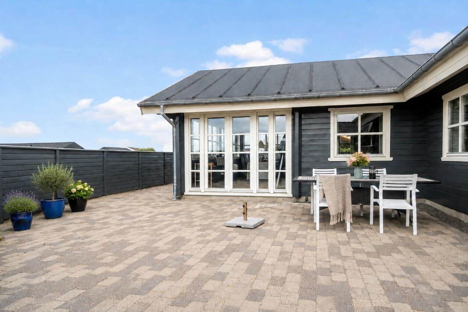 Terrasse mit Tisch, Stühlen und Pflanzen vor einem Haus mit Glasfront.
