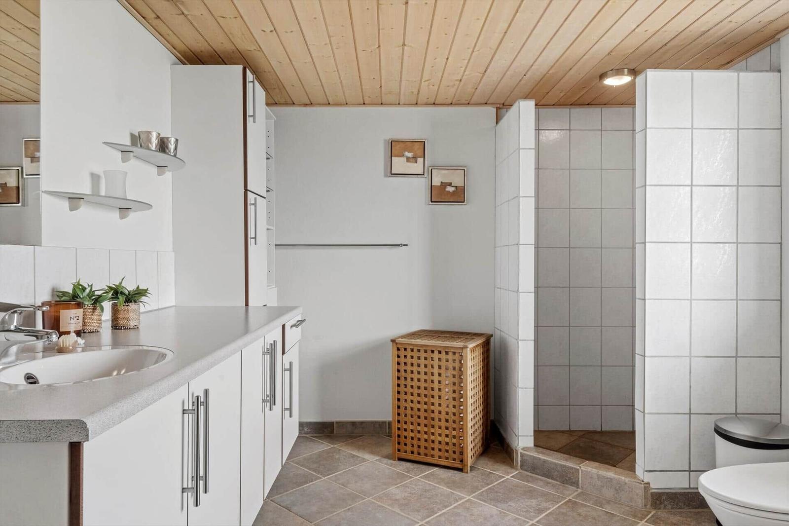 Badezimmer mit Waschbecken, Dusche und Toilette. Holzdecke und weiße Fliesen.