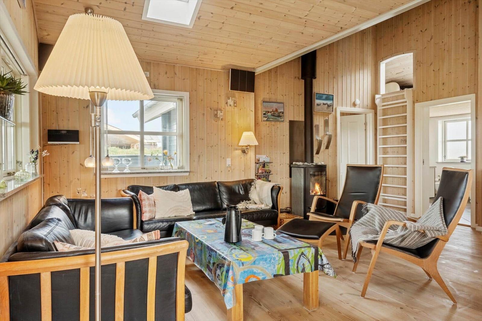 Wohnzimmer mit Holzwand, Sofa, Stühlen und Kaminofen.