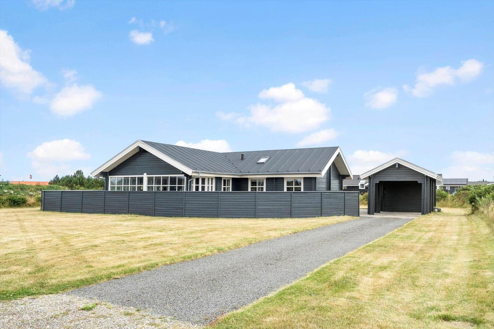 Modernes Haus mit Garage und gepflastertem Weg. Umgeben von Grünfläche unter blauem Himmel.