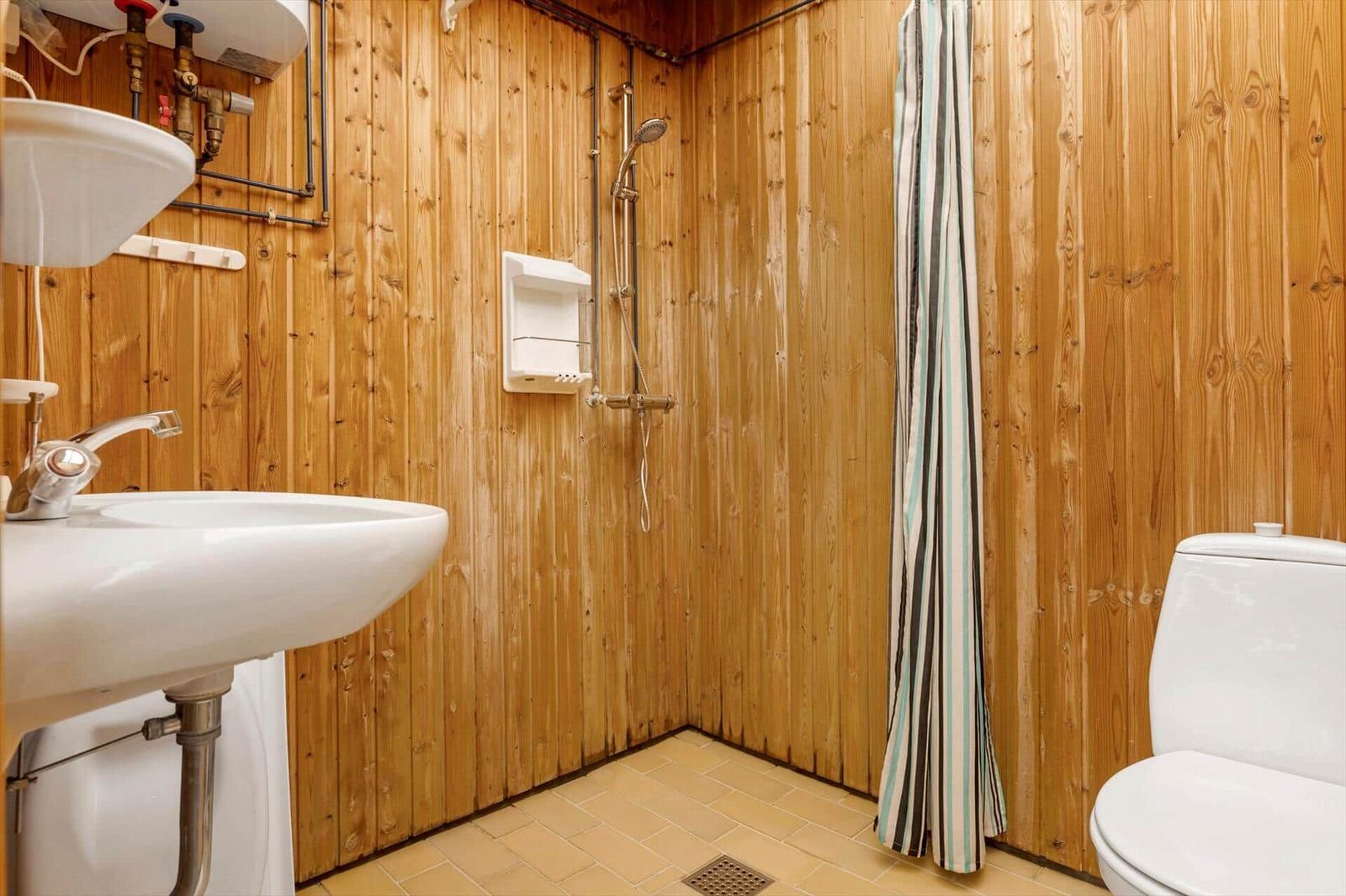 Badezimmer mit Holzwand, Waschbecken, Dusche und Toilette.