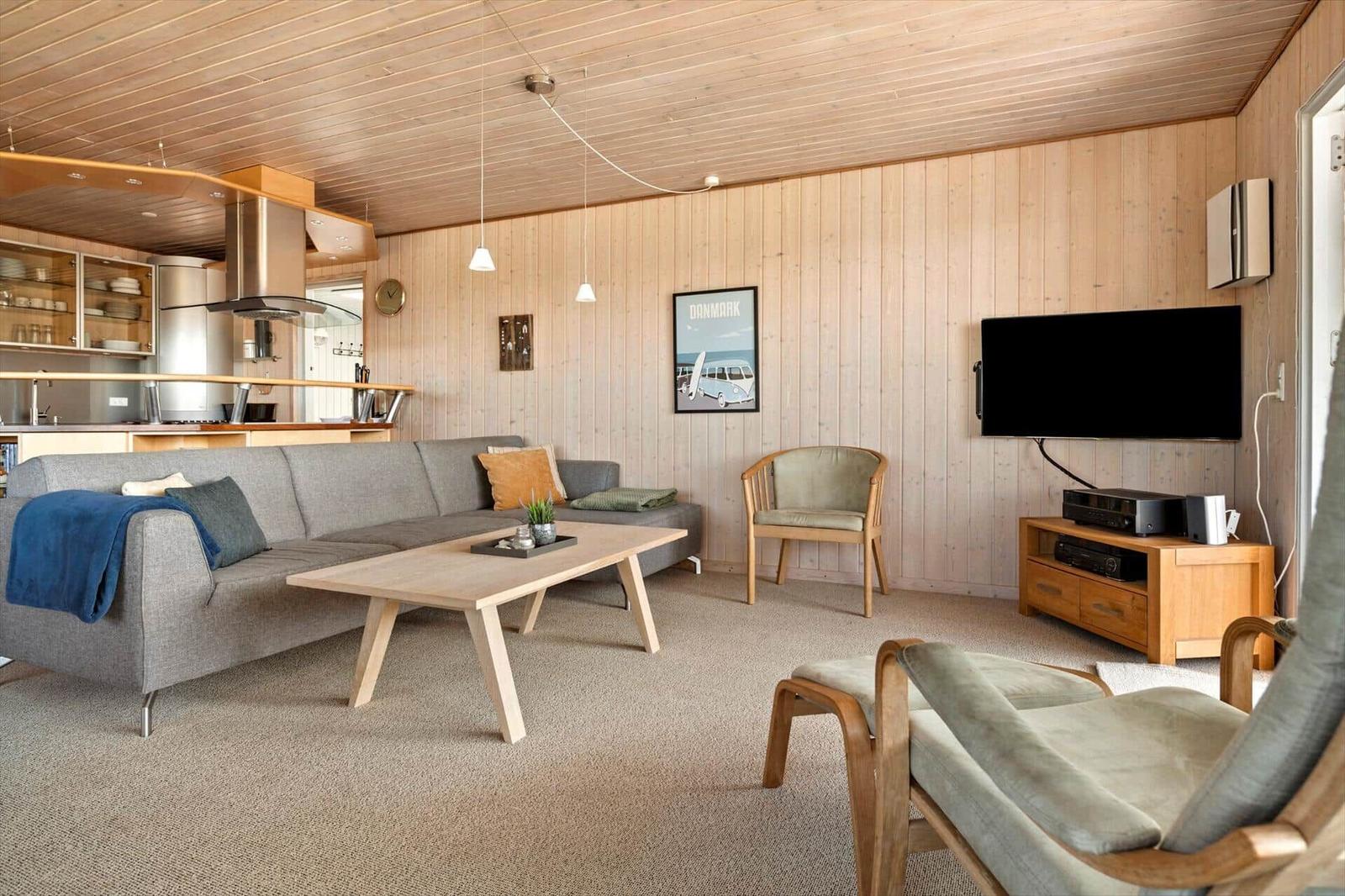 Wohnbereich mit Sofa, Couchtisch und Fernseher an Holzwand.