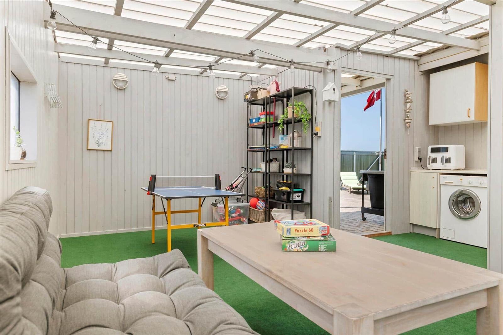 Gartenbereich mit Tischtennisplatte, Sofa und Tisch. Hintergrund: Waschmaschine und Küchenbereich.