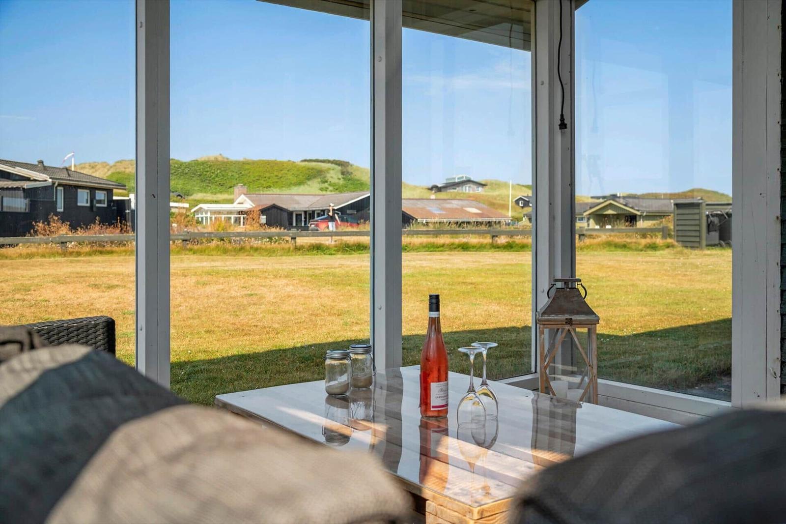 Durch große Fenster sieht man eine grüne Landschaft mit Häusern. Auf dem Tisch steht eine Flasche Rosé und Gläser.