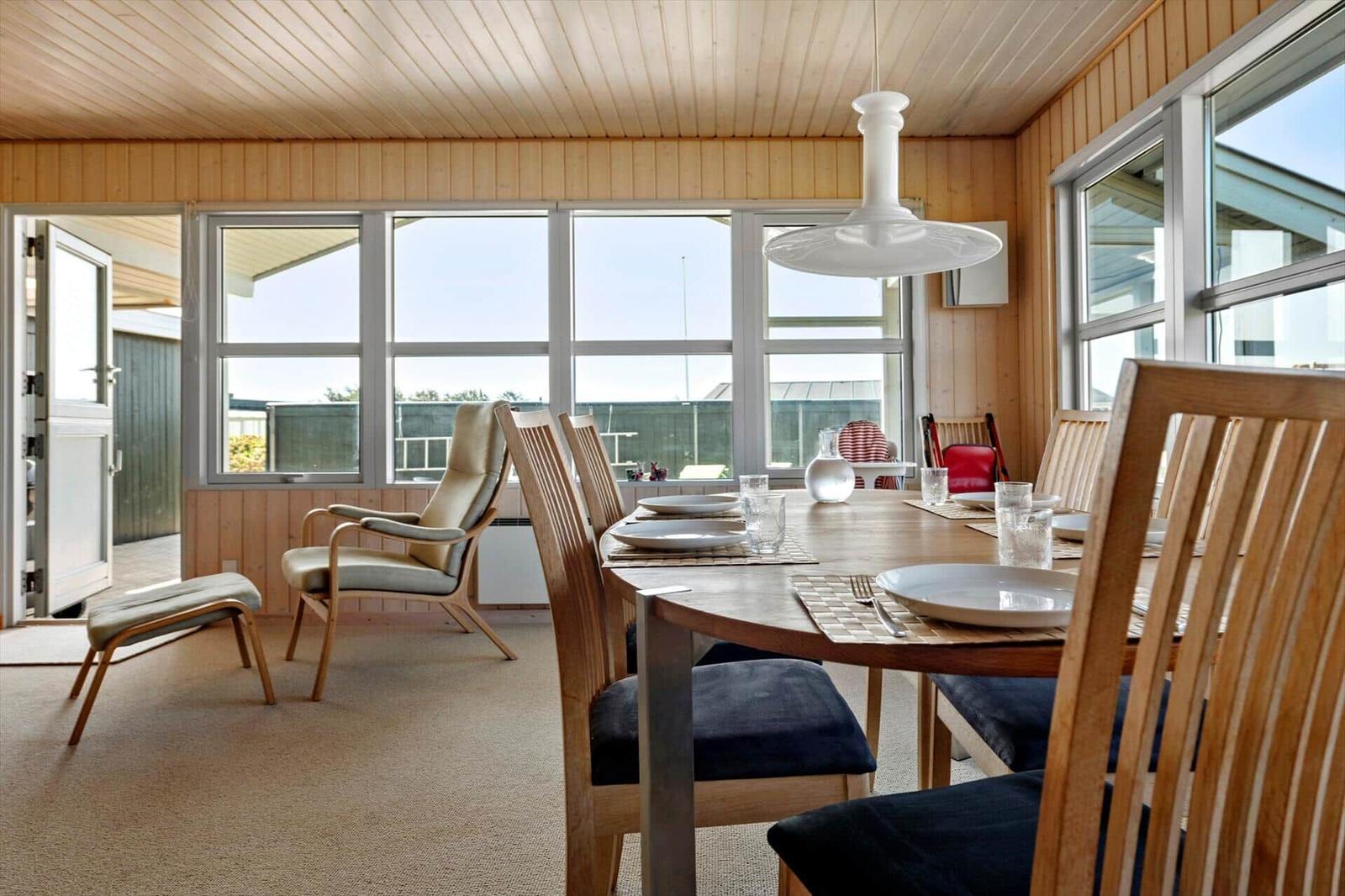 Esszimmer mit Holztisch, Stühlen und großen Fenstern. Holzwände und Decke.