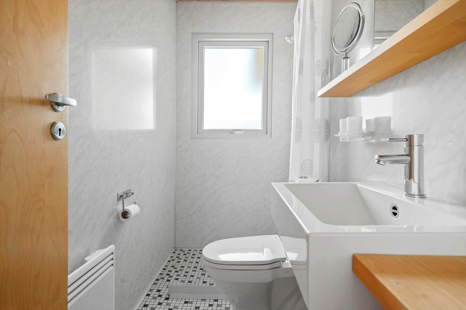 Badezimmer mit Toilette, Waschbecken und Dusche. Holzakzente und Mosaikboden.