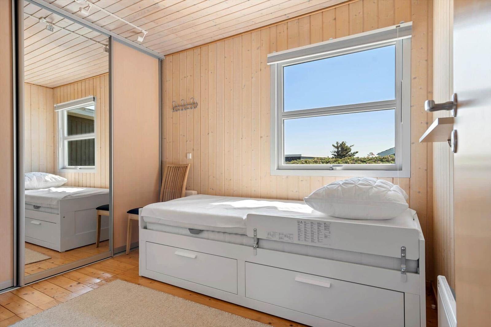 Schlafzimmer mit weißem Bett, Holzwand und Fenster mit Blick.
