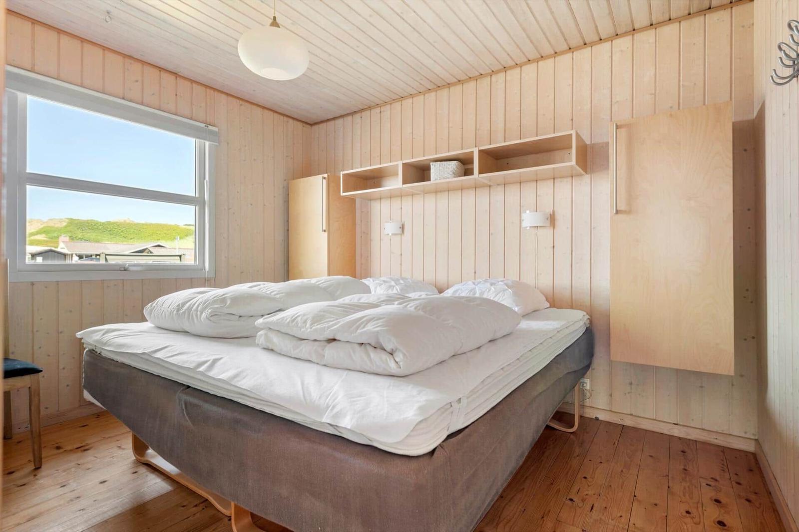 Schlafzimmer mit Holzwand, Bett und Fenster zum See.
