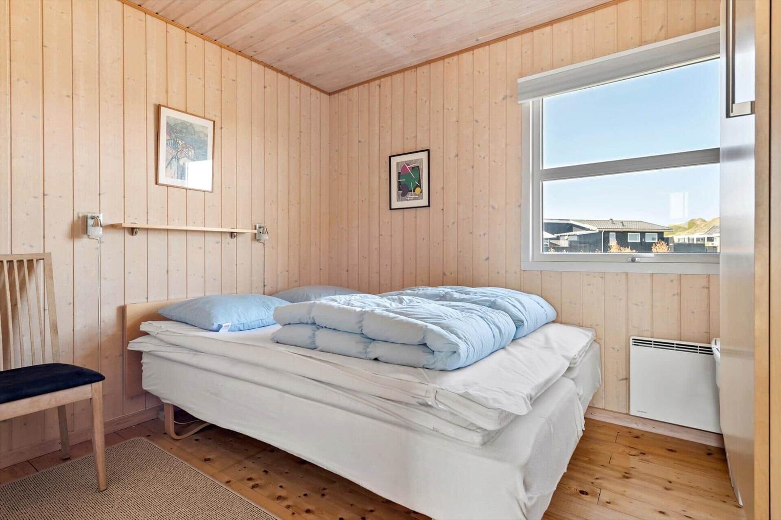 Schlafzimmer mit Holzwand, Bett, Stuhl und Fenster.