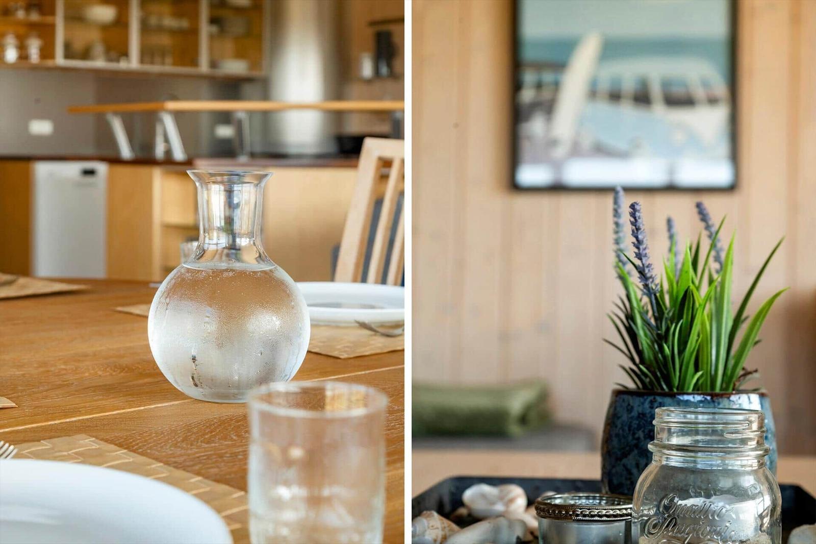 Holztisch mit Wasserglas und Keramikbecher. Wandbild mit Strandmotiv und Pflanze im Vordergrund.