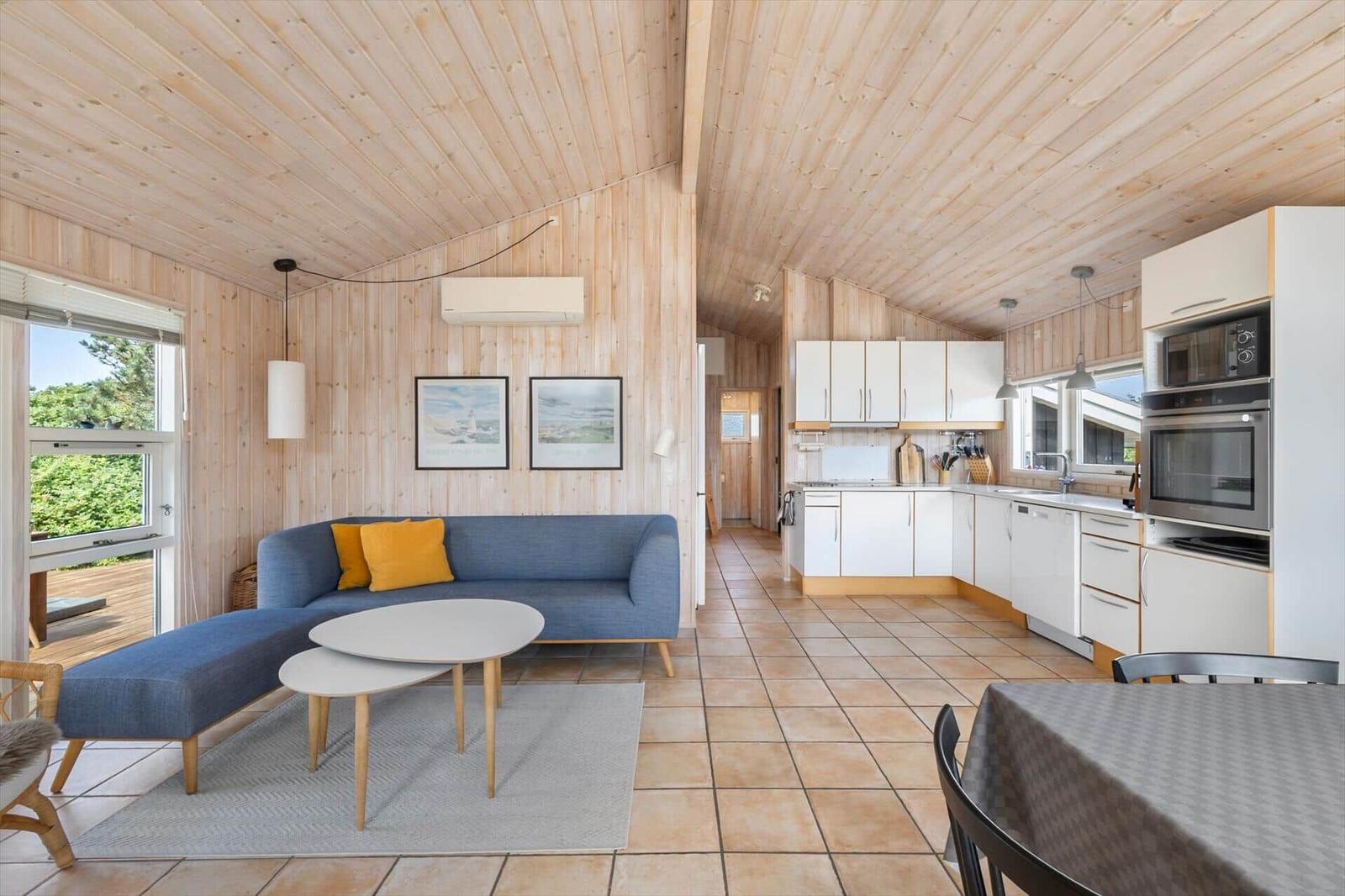 Living and kitchen area with wooden walls, sofa, table, and modern kitchen unit.