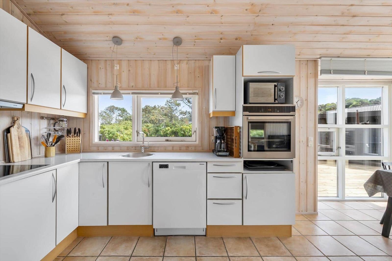 Kitchen with white cabinets, stainless steel appliances, and wood paneling. View of garden through window.