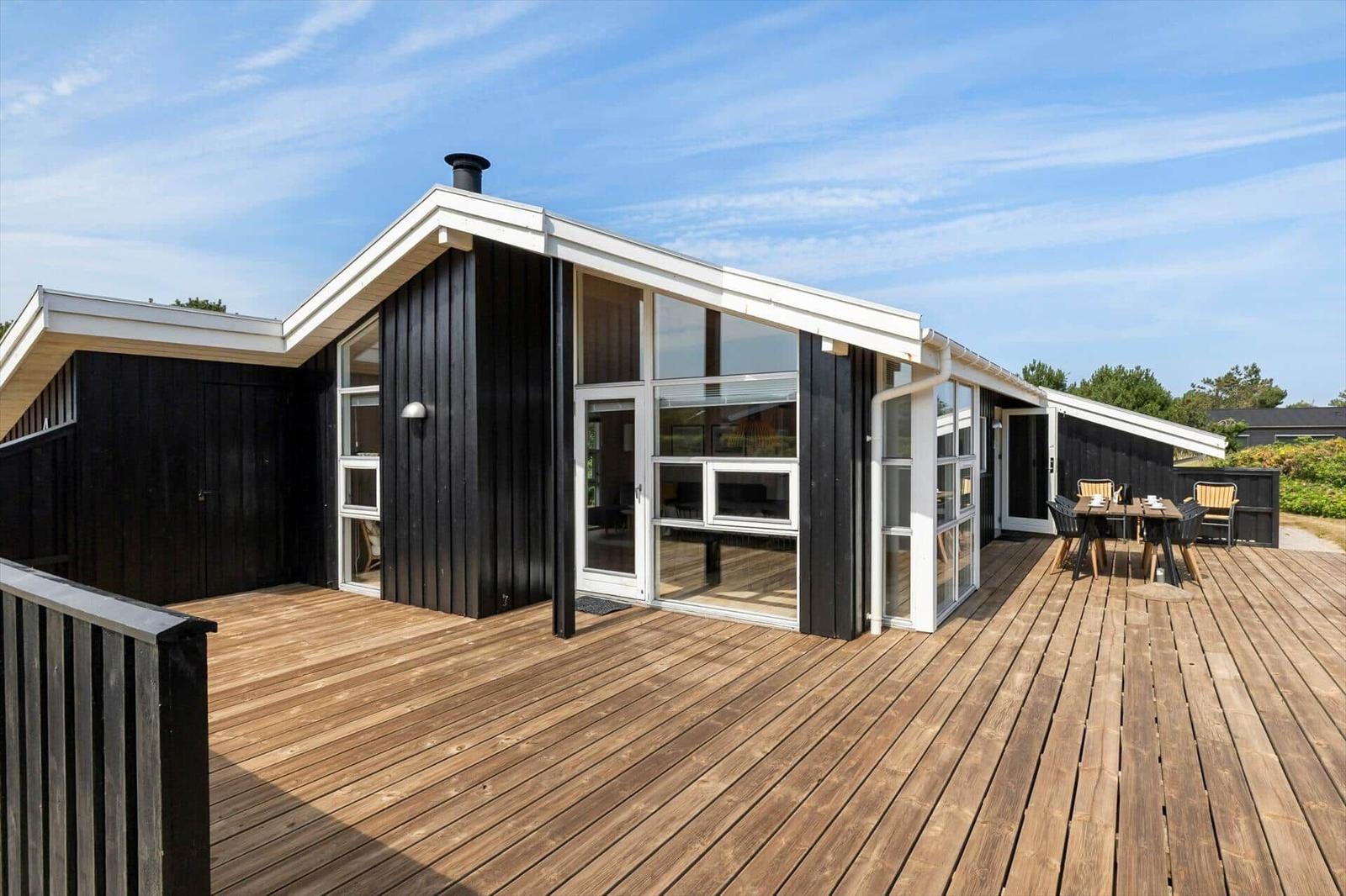 Modern wooden cabin with large terrace area and outdoor table.