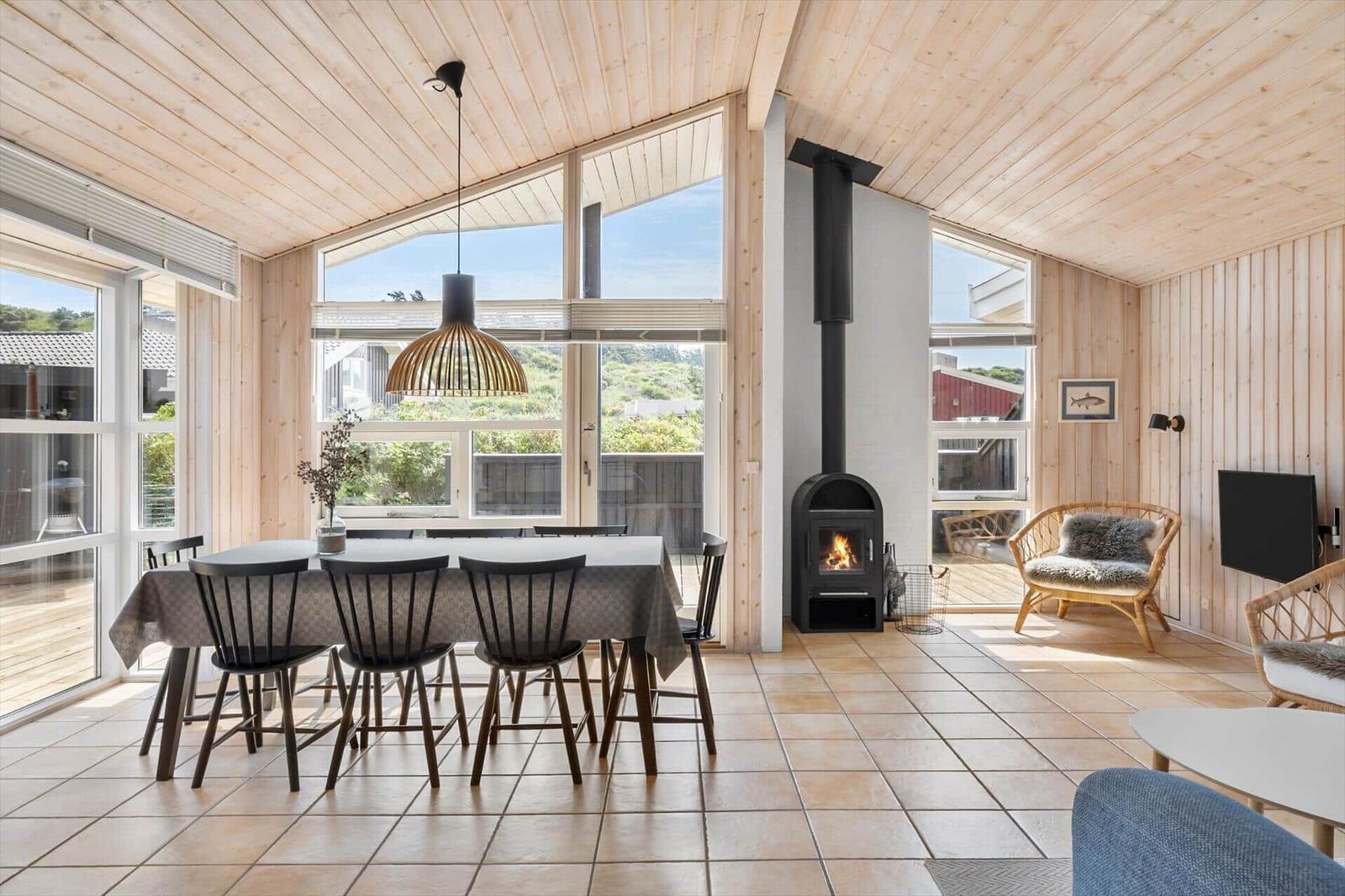 Dining area with table, chairs, and wood stove. Wooden walls and large windows.