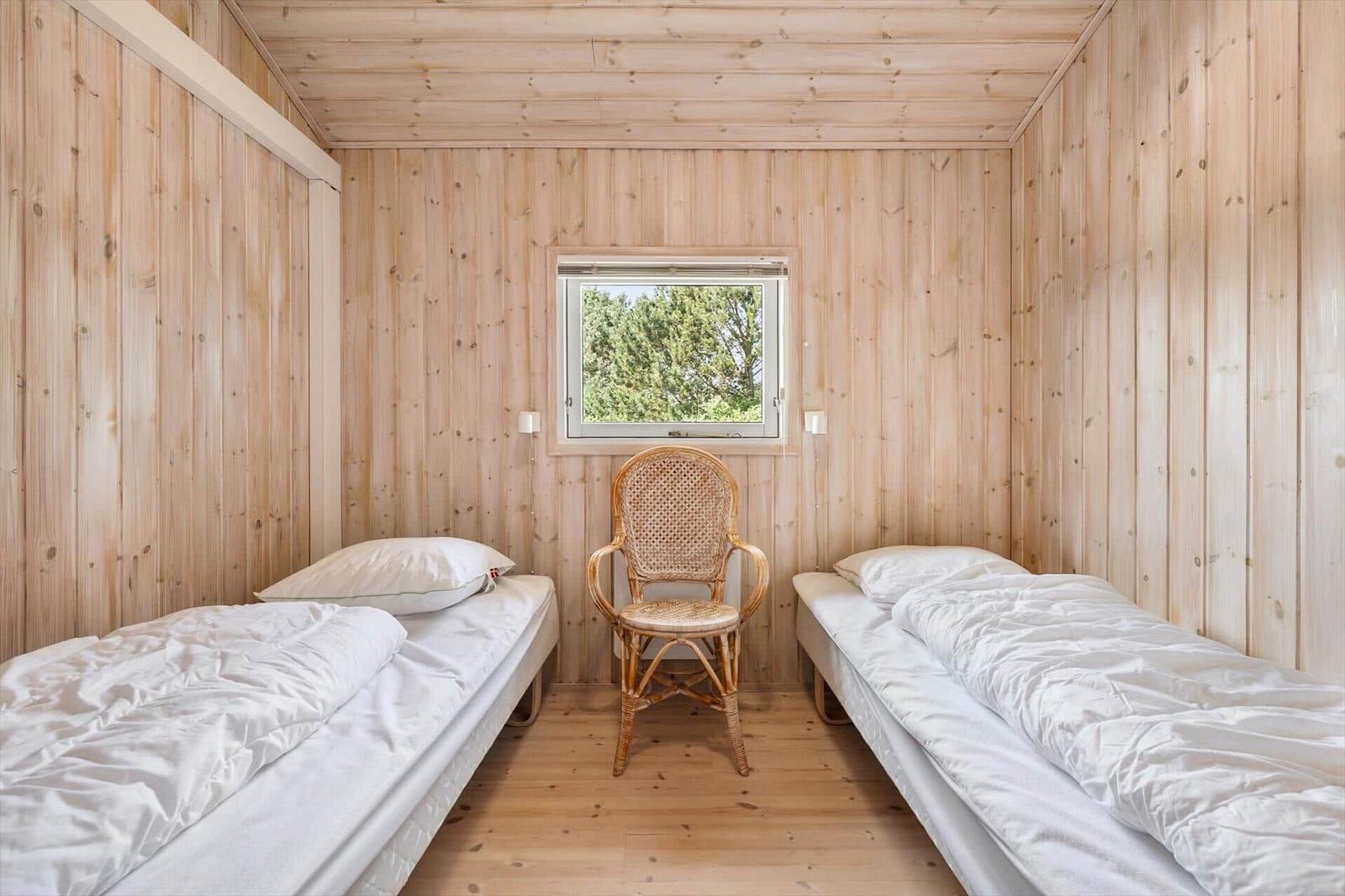 Two beds and a chair in a wood-paneled room with a window.