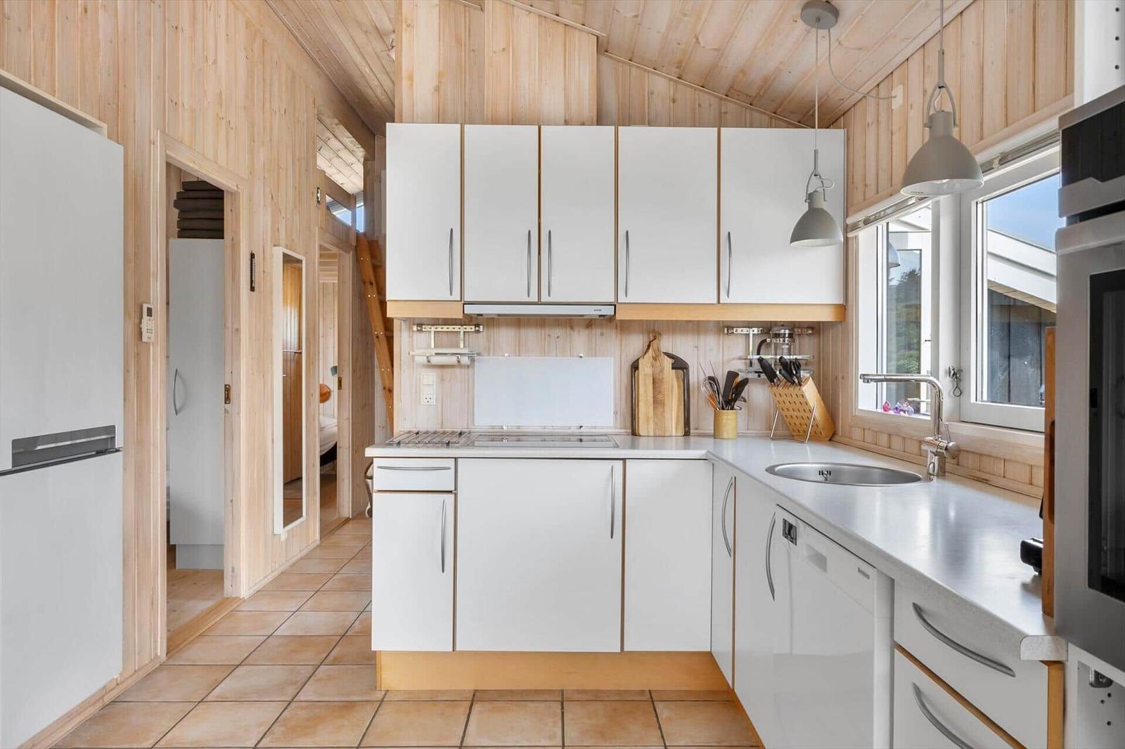 Kitchen with white cabinets, stainless steel sink, and wooden wall cladding.