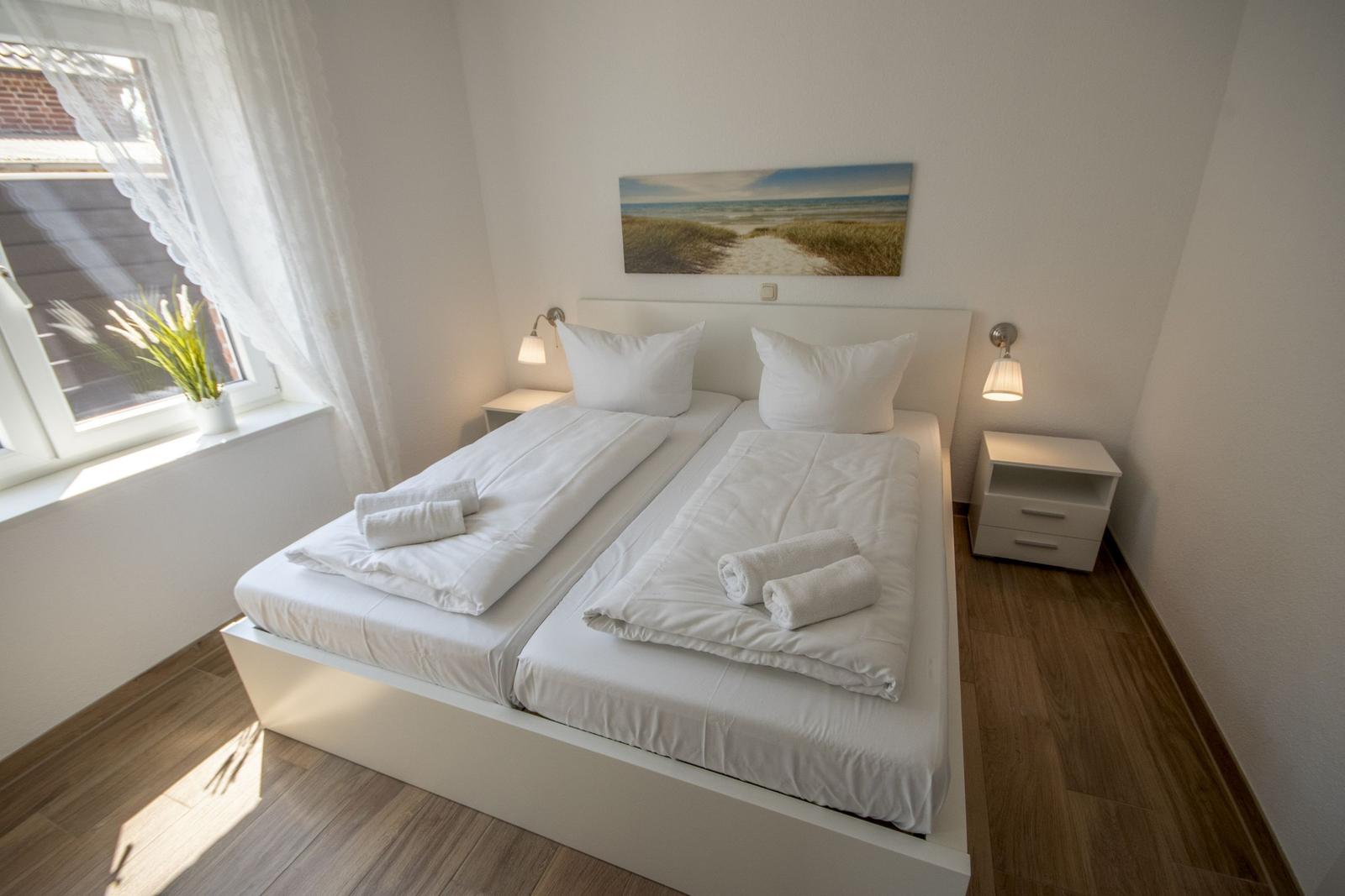 Schlafzimmer mit Doppelbett, zwei Nachttischen und Fenster mit weißen Vorhängen.