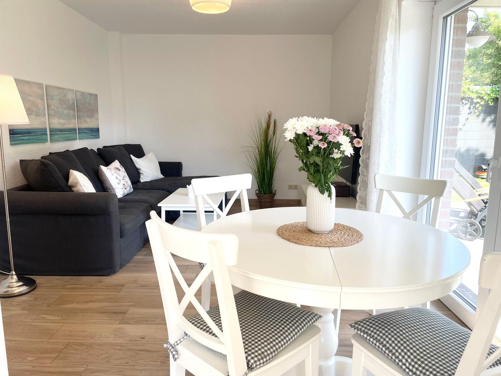 Esszimmer mit runder Tisch und weißen Stühlen. Wohnbereich mit Sofa und Fenster.