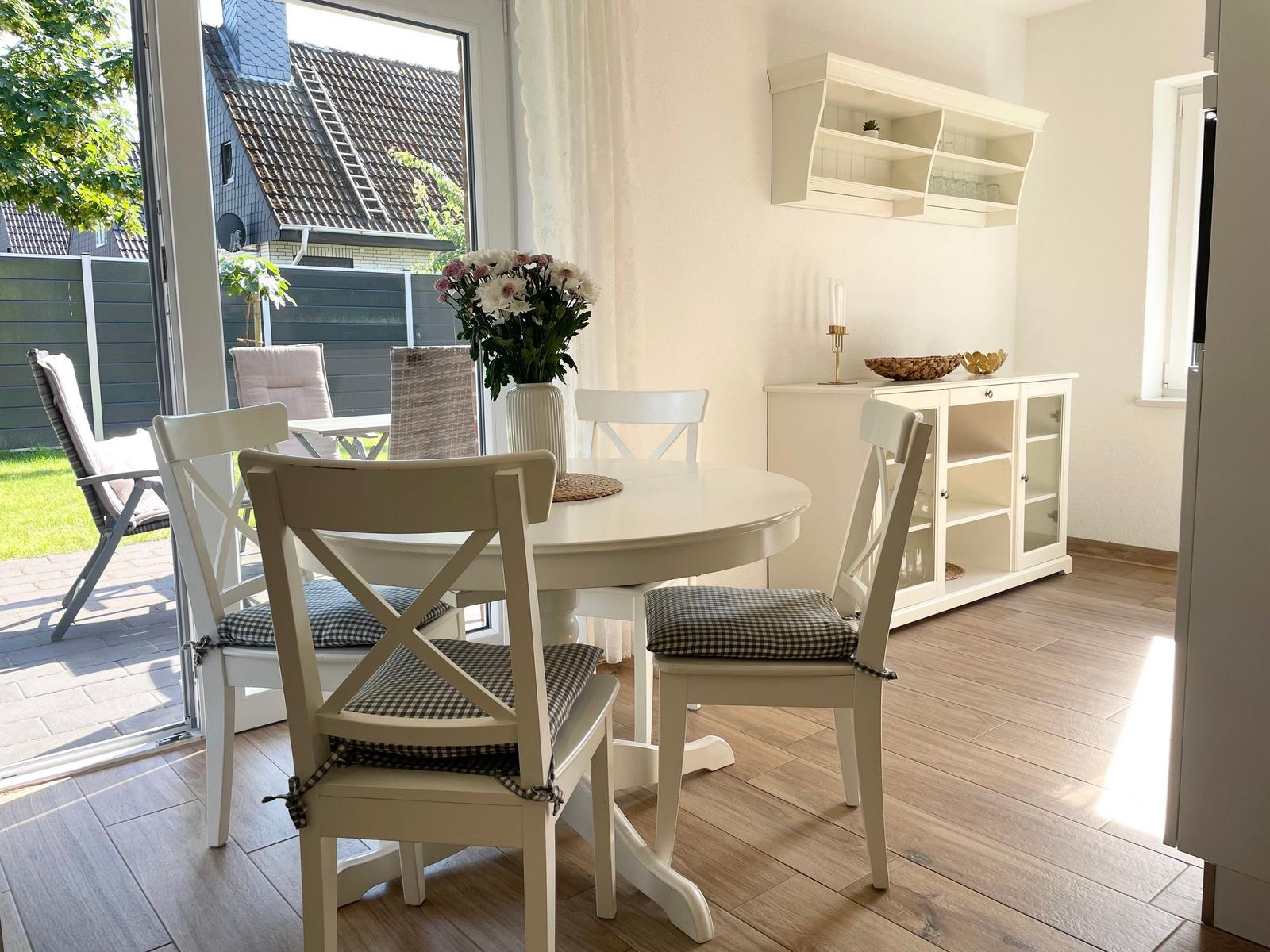 Esszimmer mit weißem Tisch, Stühlen und Schrank. Durchgang zur Terrasse mit Garten.