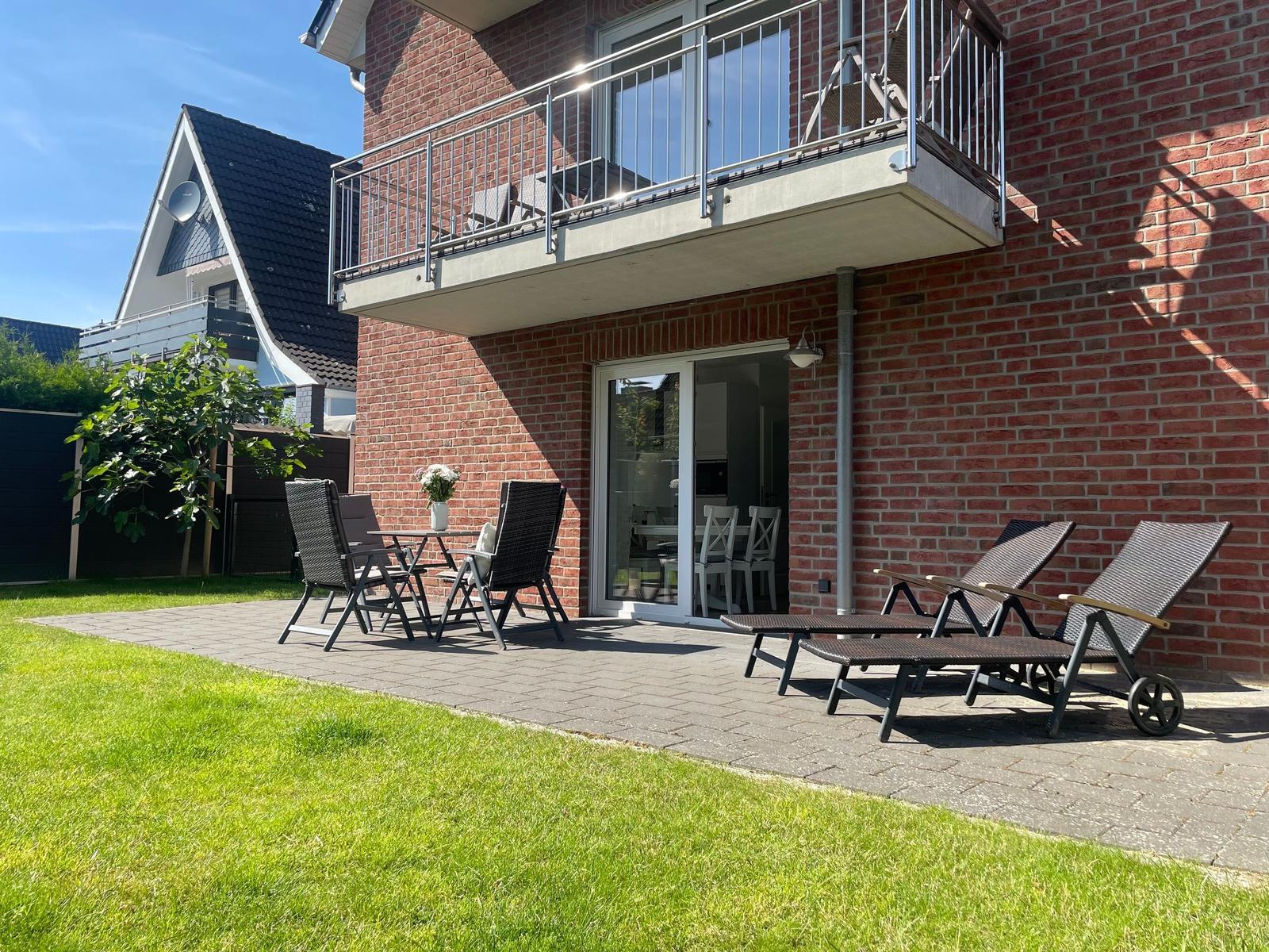 Terrasse mit Liegen und Tisch. Hinterhof mit Gras und Balkon.