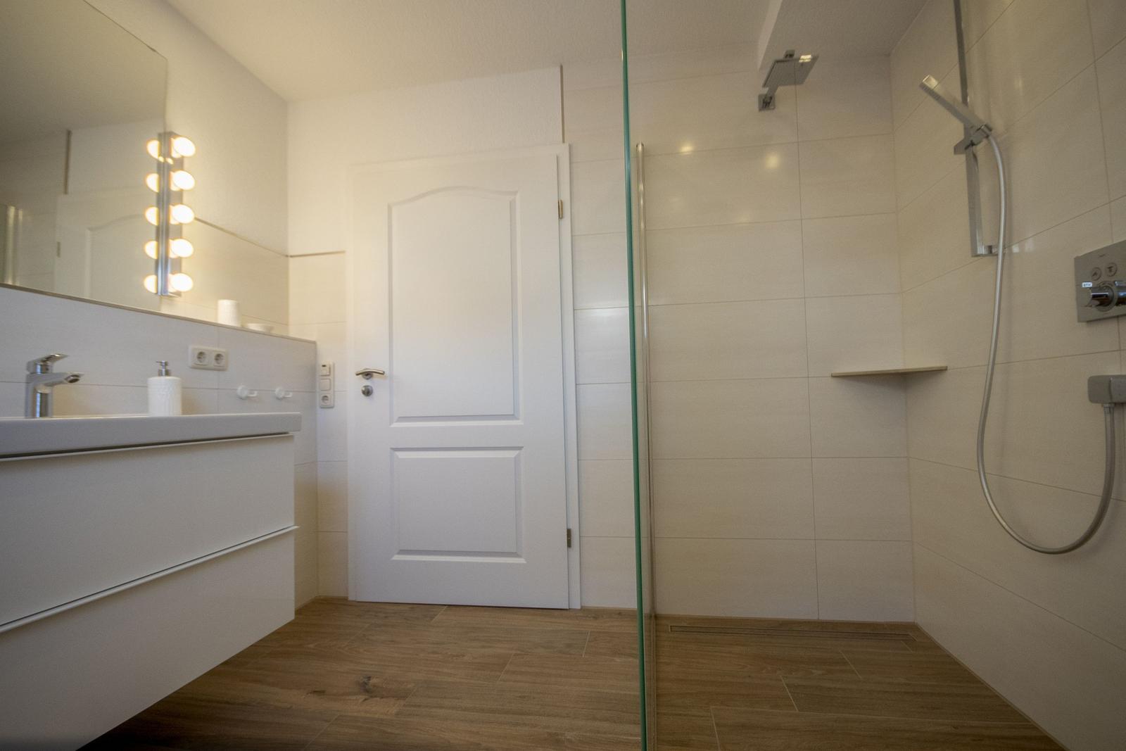 Badezimmer mit Dusche, Waschbecken und Spiegel mit Lichtern.
