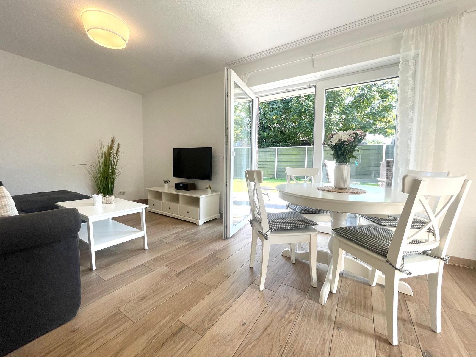 Wohn- und Essbereich mit Esstisch, Sofa und TV. Terrasse mit Gartenansicht.