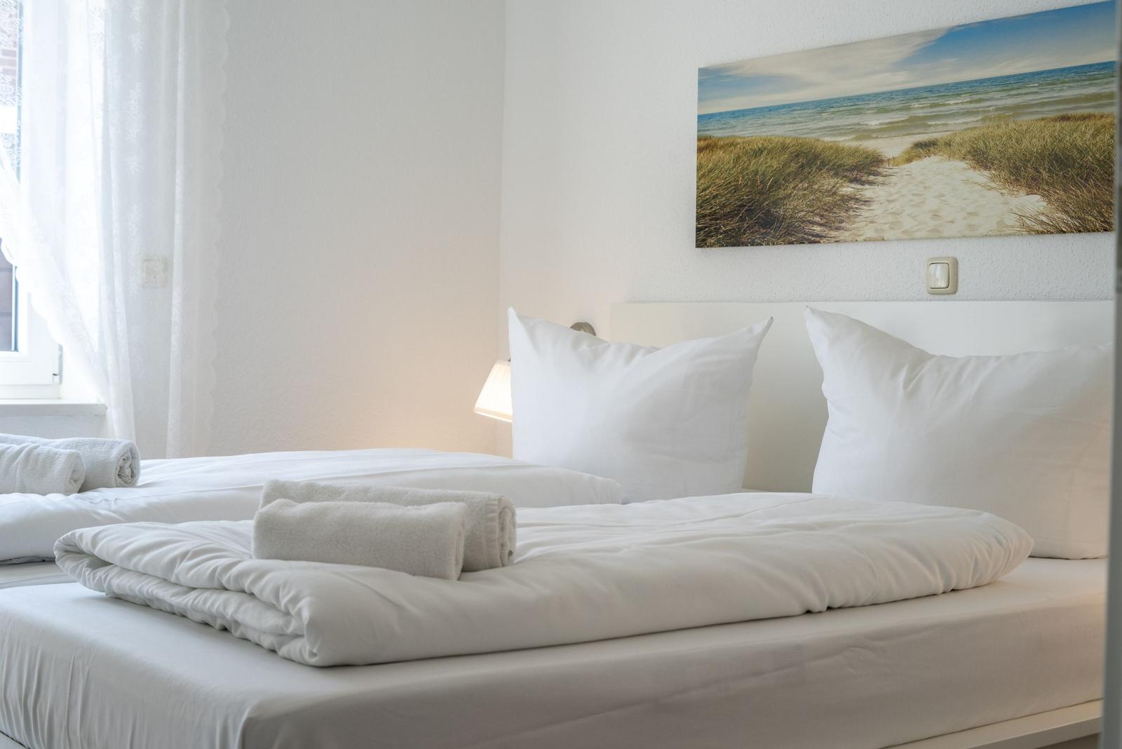 Ein Bett mit weißen Laken und Handtüchern. An der Wand hängt ein Strandbild.