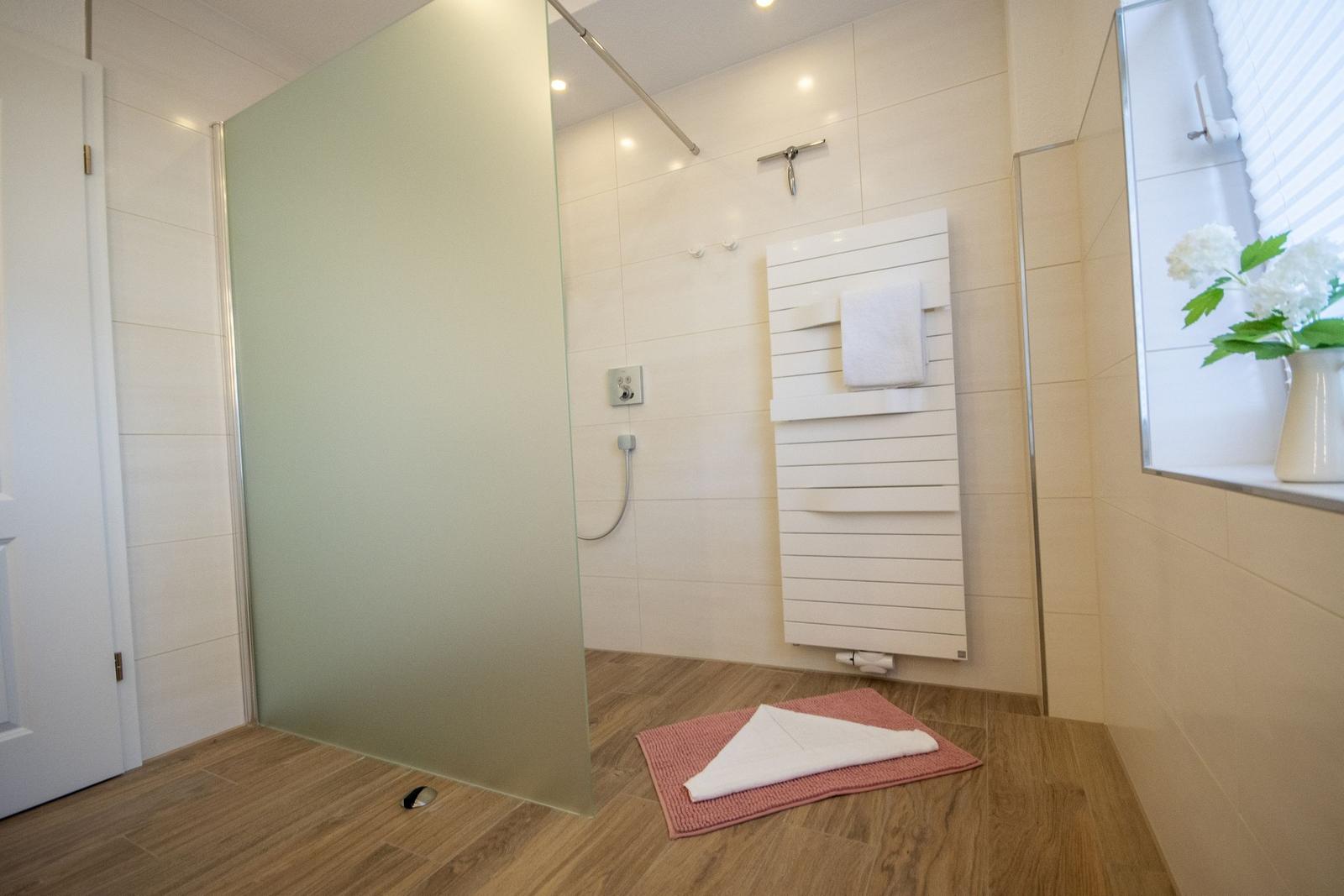 Dusche mit Duschbrause, Handtuchhalter und Fenster mit Blumen.