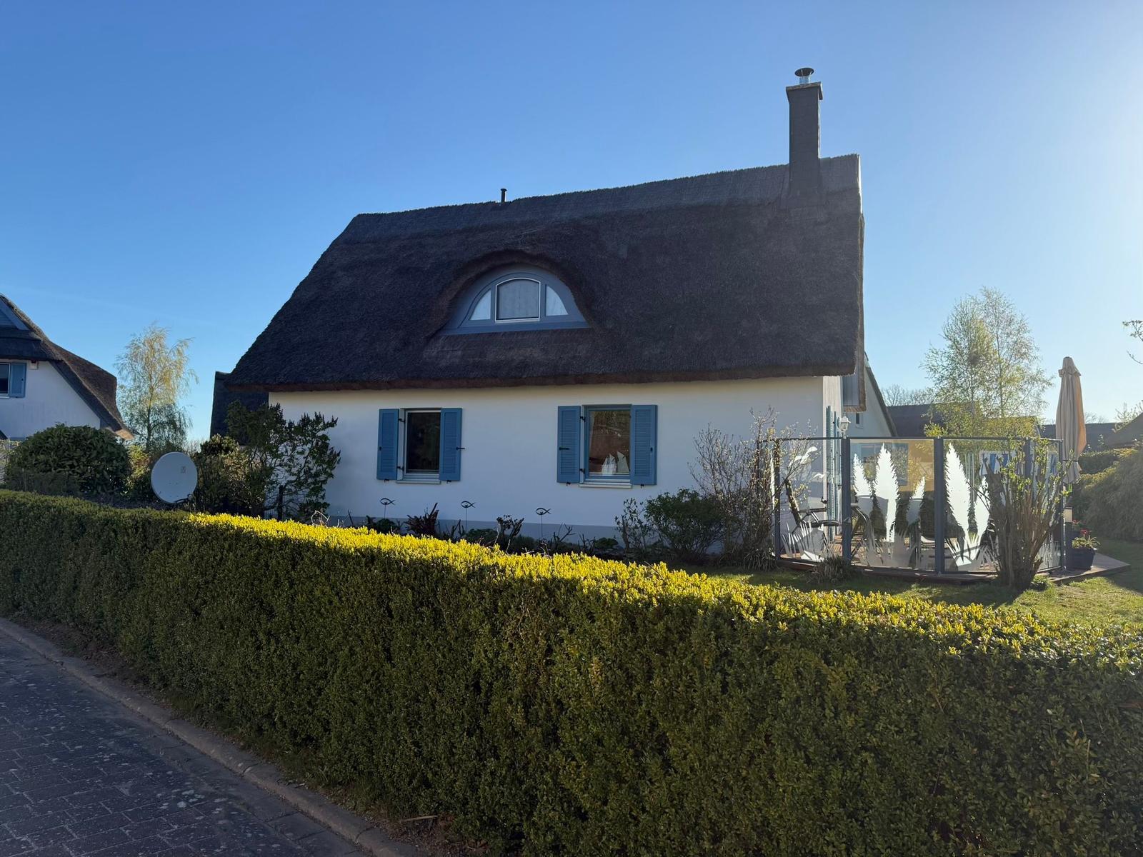 Wohnhaus mit Strohdach, blauen Fensterläden und Garten mit Terrasse.