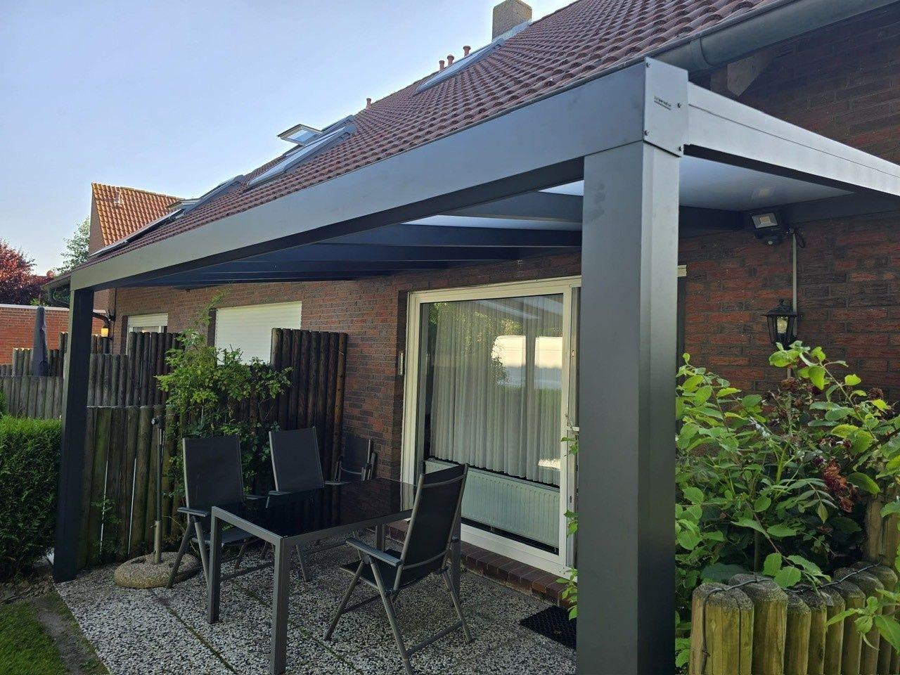 Terrasse mit Sitzgruppe unter Pavillon, umgeben von Pflanzen und Holzzaun.