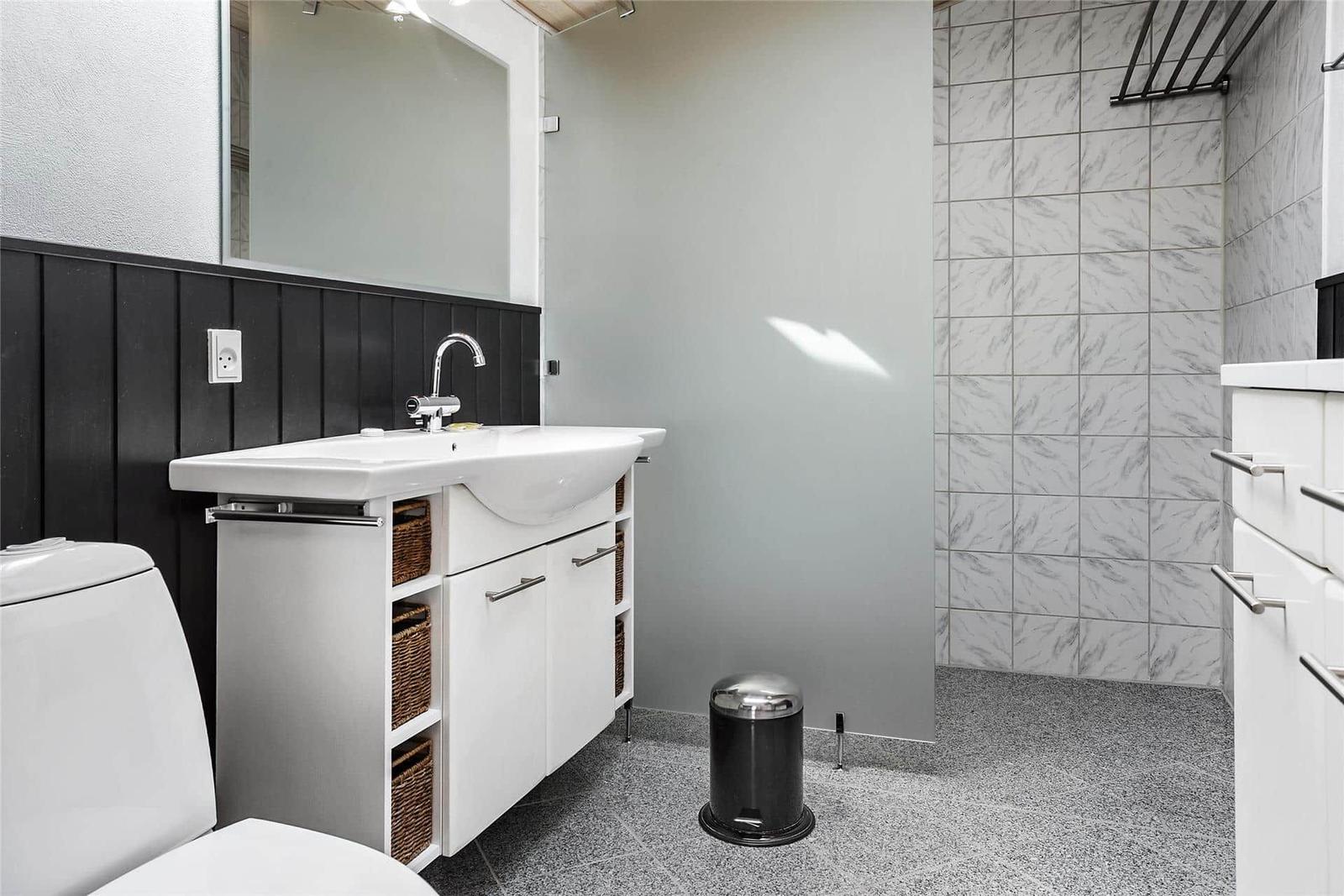 Badezimmer mit Waschbecken, Toilette und Dusche. Weiße Schränke, schwarze Wandverkleidung und Marmorfliesen.