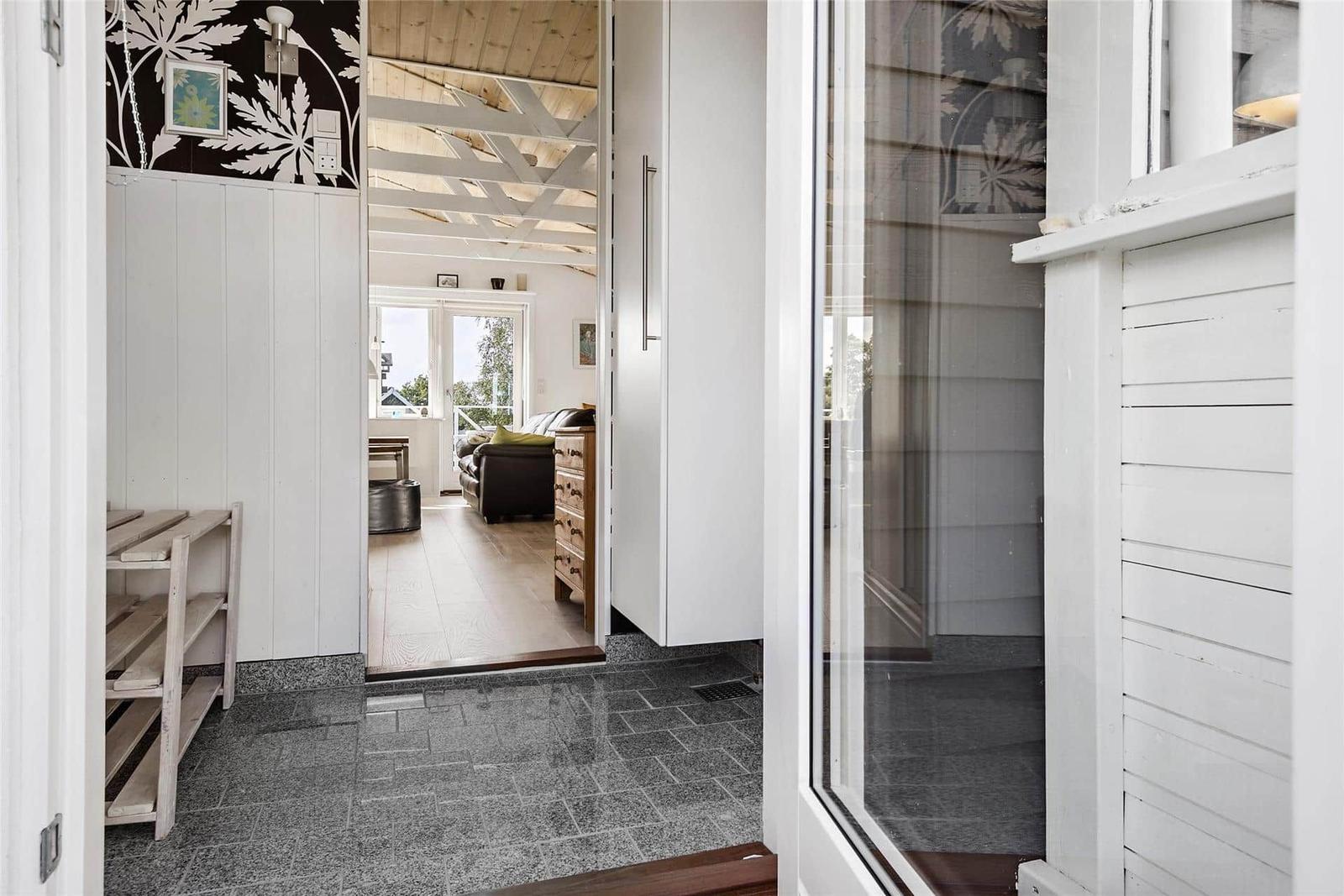 Eingangsbereich mit grauem Fliesenboden und Blick in Wohnzimmer mit Holzboden und Sofa.