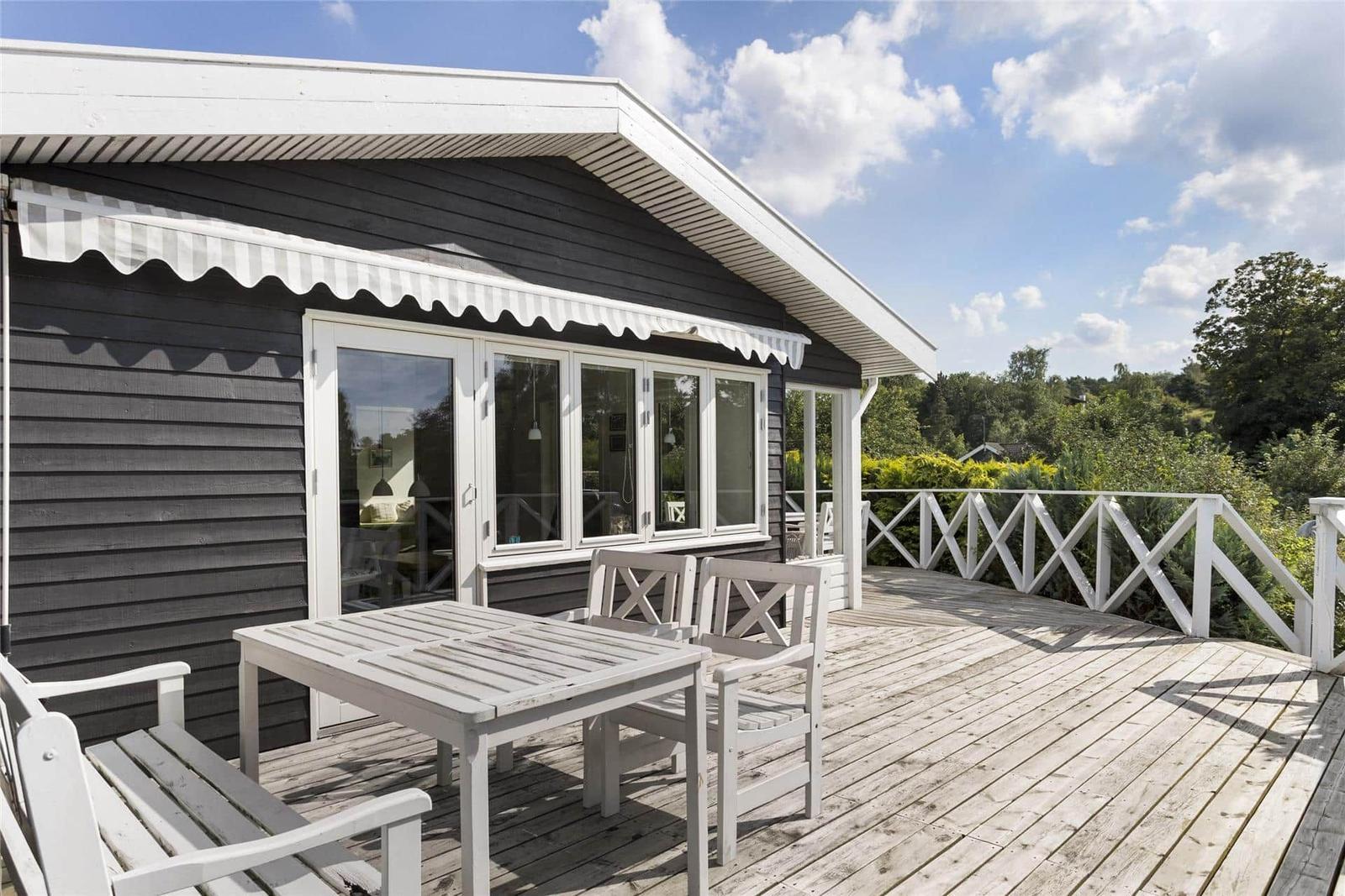 Terrasse mit Tisch und Stühlen vor einem Haus mit weißen Fenstern und Balkon.