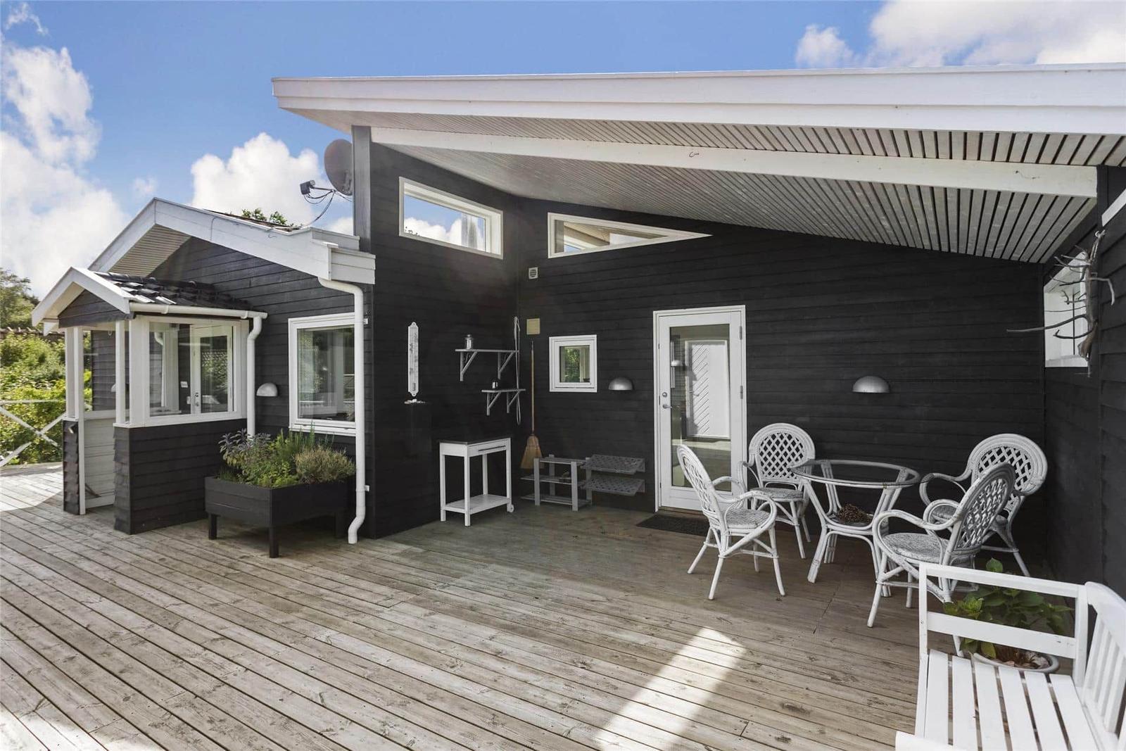 Terrasse mit weißen Stühlen und Tisch vor schwarzem Haus mit Dachüberstand.