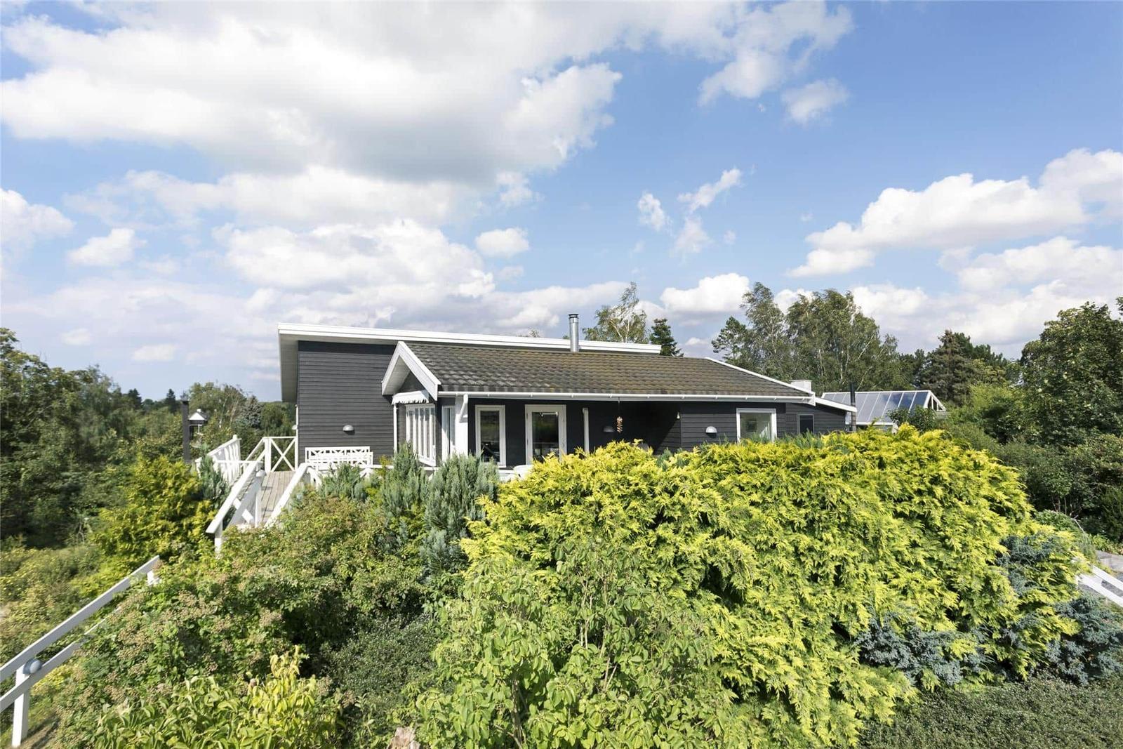Ein modernes Haus mit weißem Geländer und grüner Umgebung unter blauem Himmel.