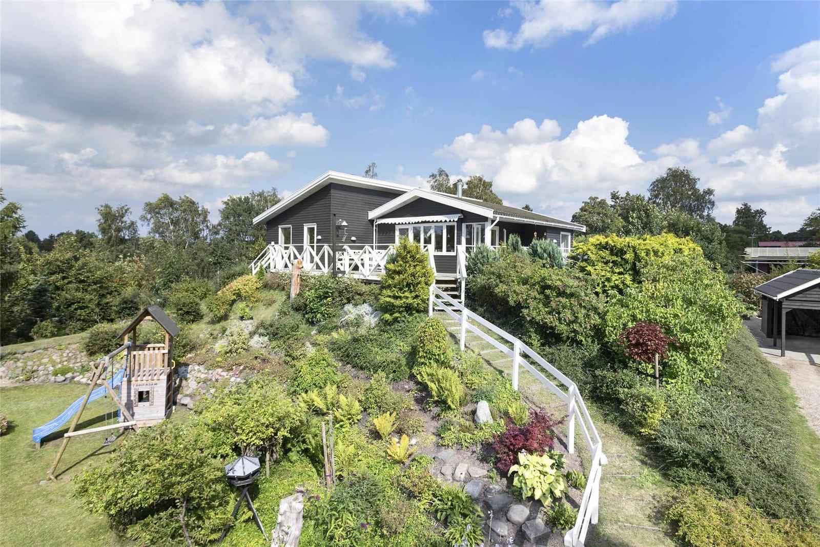 Ein dunkel gestrichenes Haus mit weißem Geländer und Spielplatz im Garten.