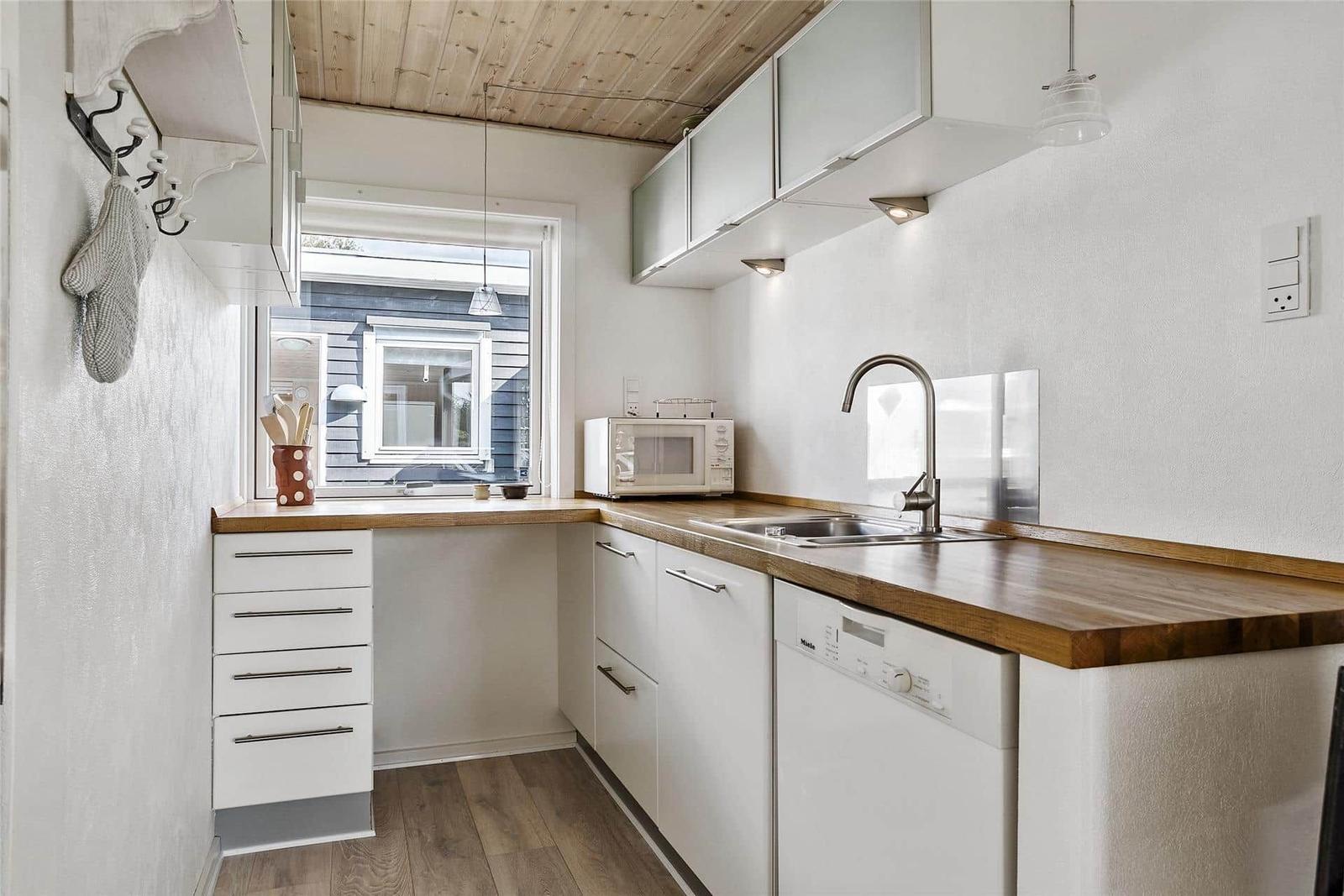 Küche mit Holzoberfläche, weißen Schränken und Fensterblick