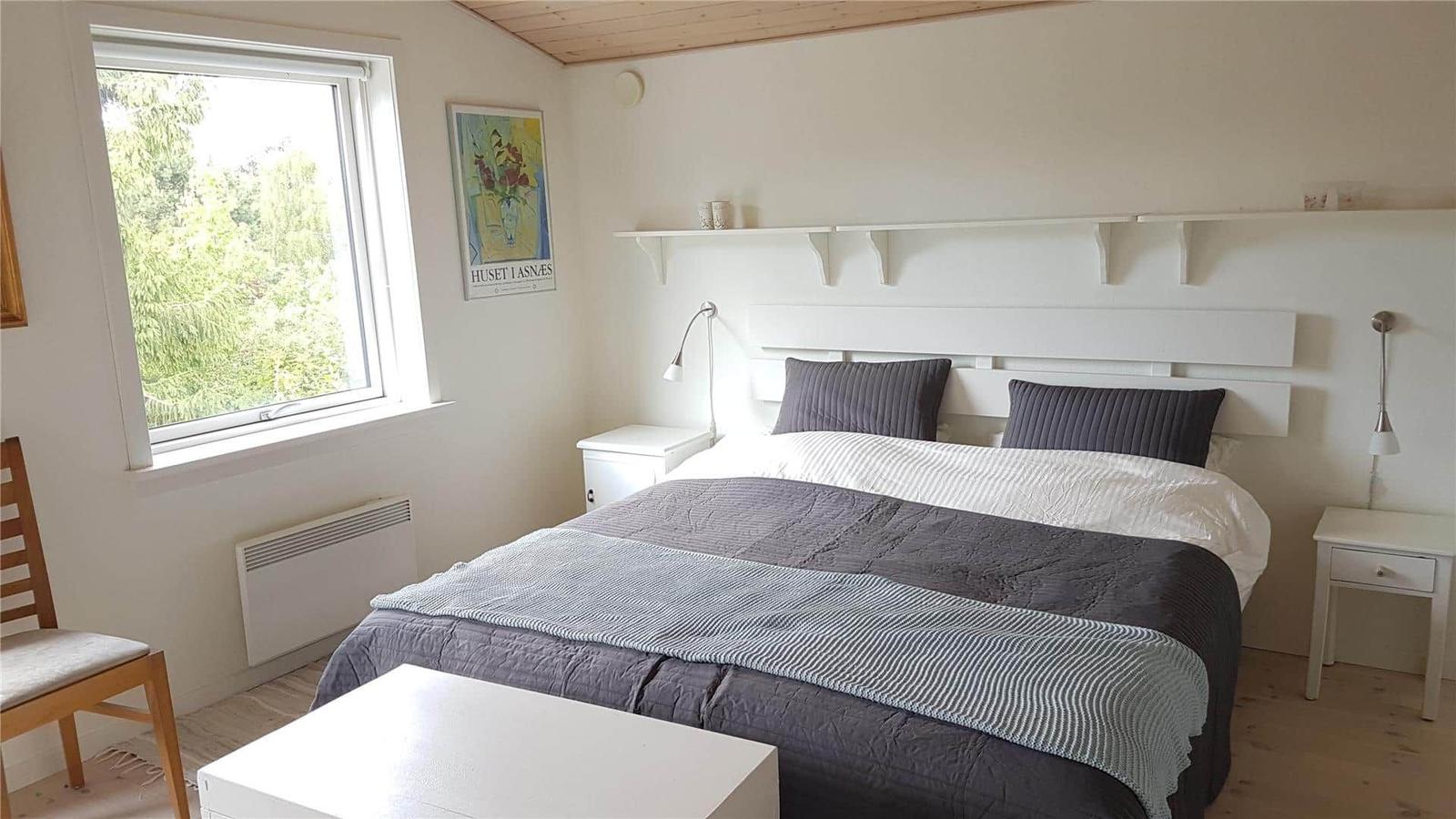 Schlafzimmer mit Bett, Nachttischen und Fenster zur grünen Umgebung.