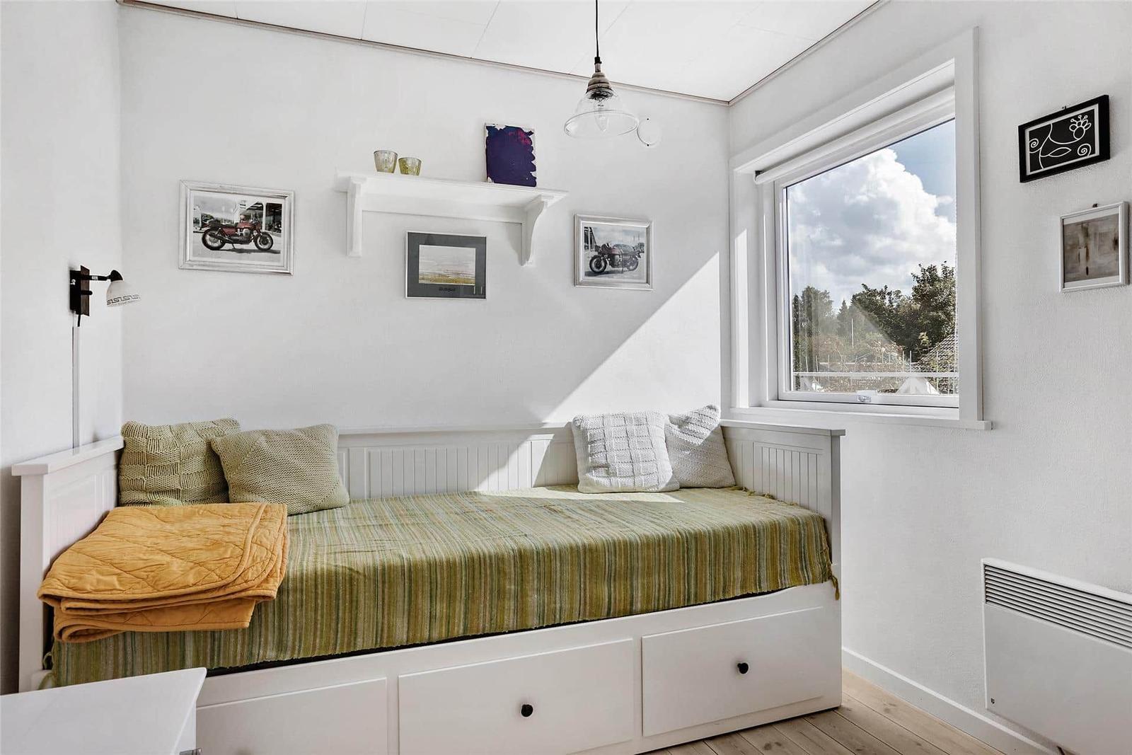 Ein Schlafzimmer mit Fenster, Bett und Wandregal mit Bildern.