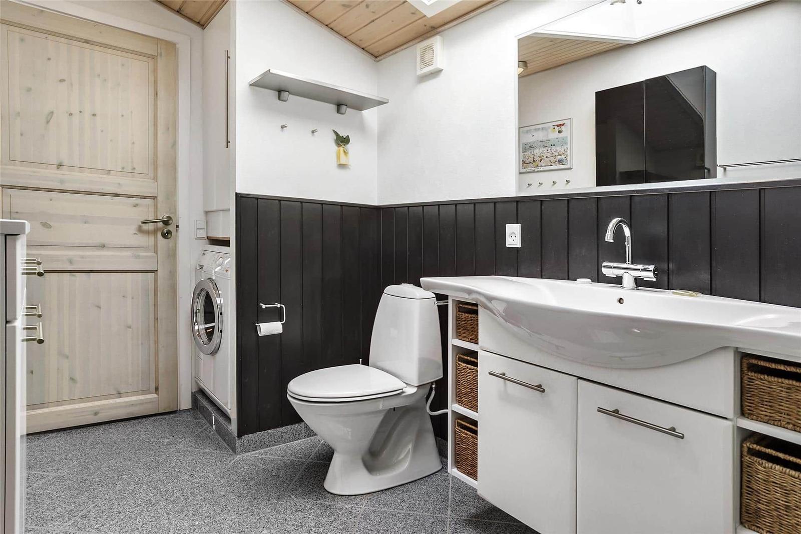 Badezimmer mit Toilette, Waschbecken und Waschmaschine. Holzwand und Spiegel.