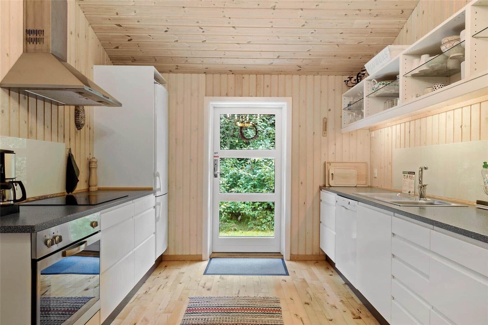Kitchen with white cabinets, wooden walls, and door to the garden.