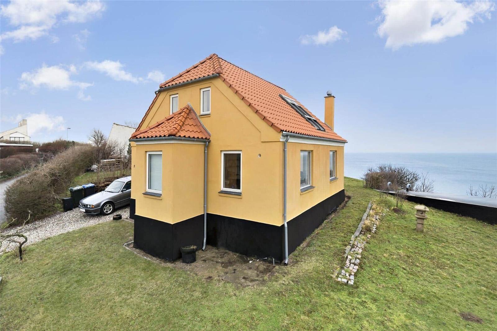 Gelbes Haus mit rotem Dach und Fenstern, umgeben von Gras und Bäumen.