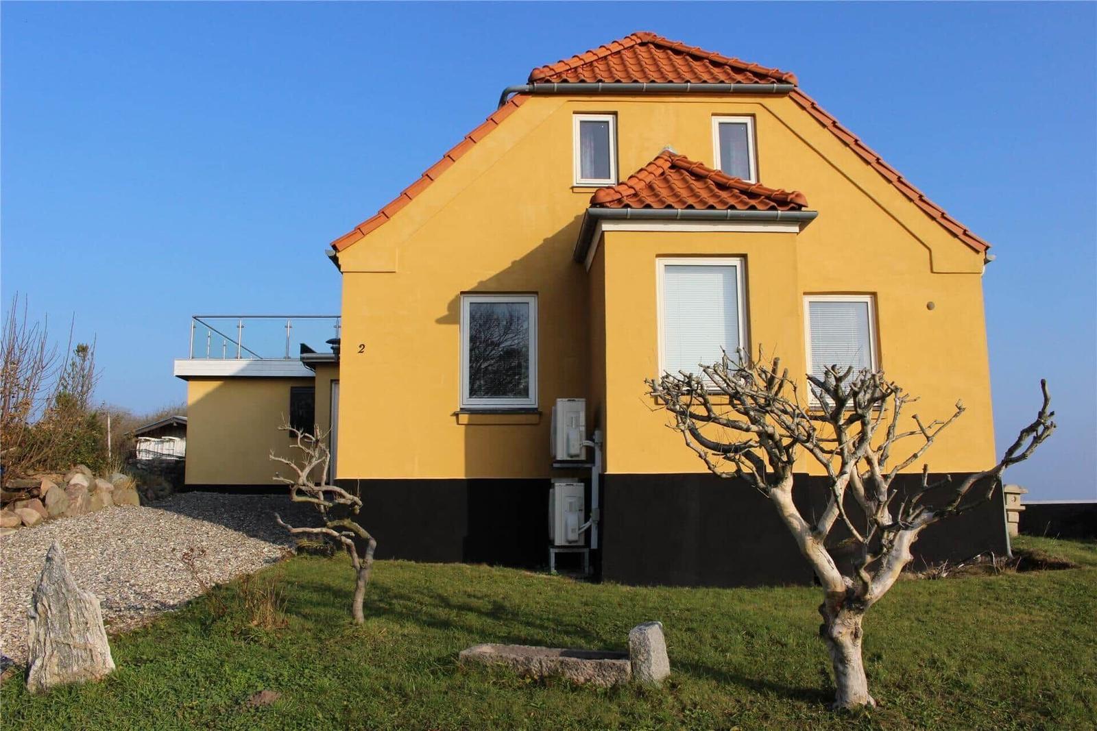 Grüner Hang mit Blick aufs Meer, gelbes Haus, Holzgeländer und Stein.
